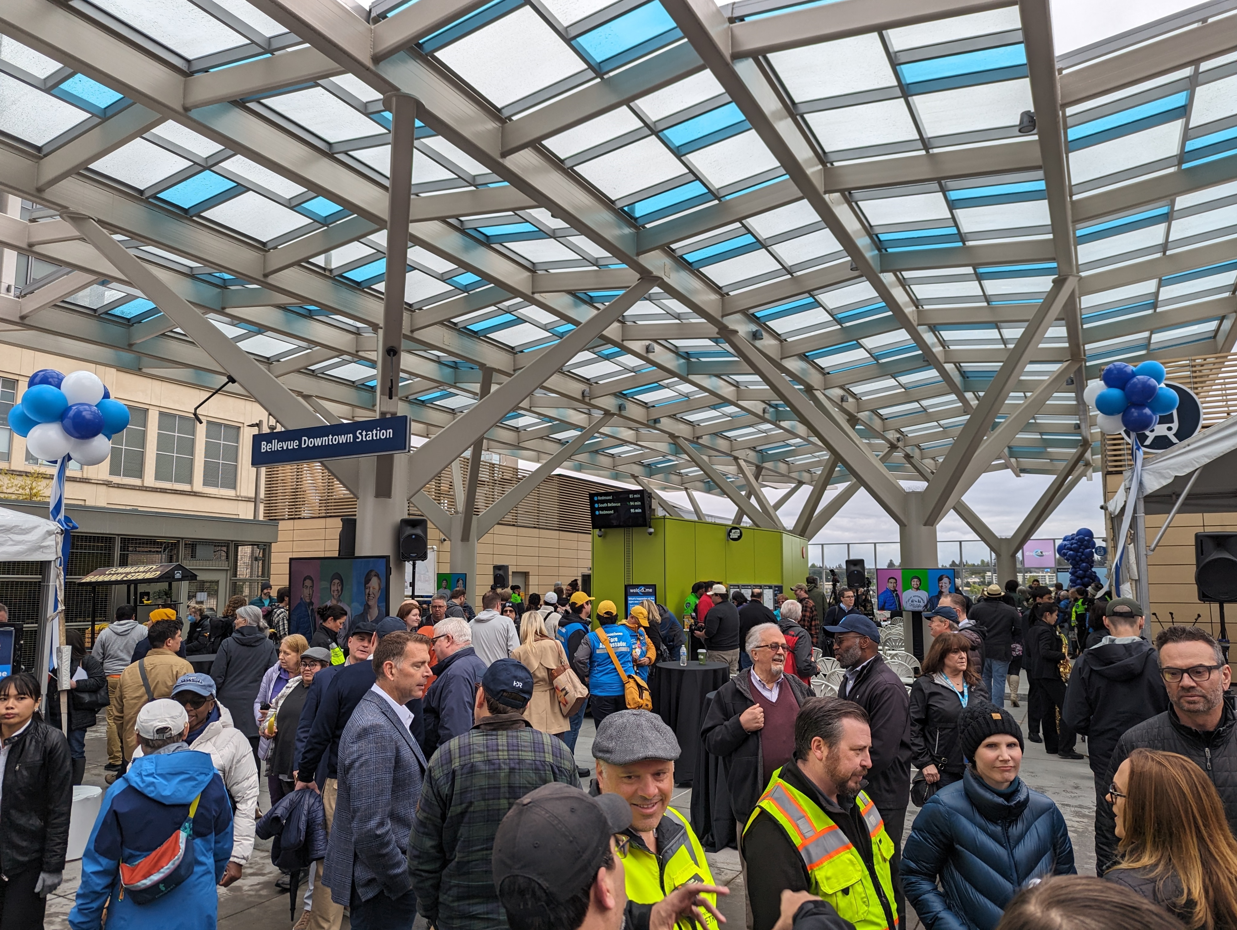 Crowd gathered under a glass-and-steel canopy at a light rail station with balloons.