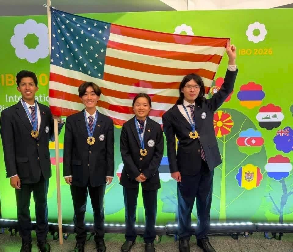 Four young people in dark blazers wearing gold medals pose in front of an IBO backdrop.