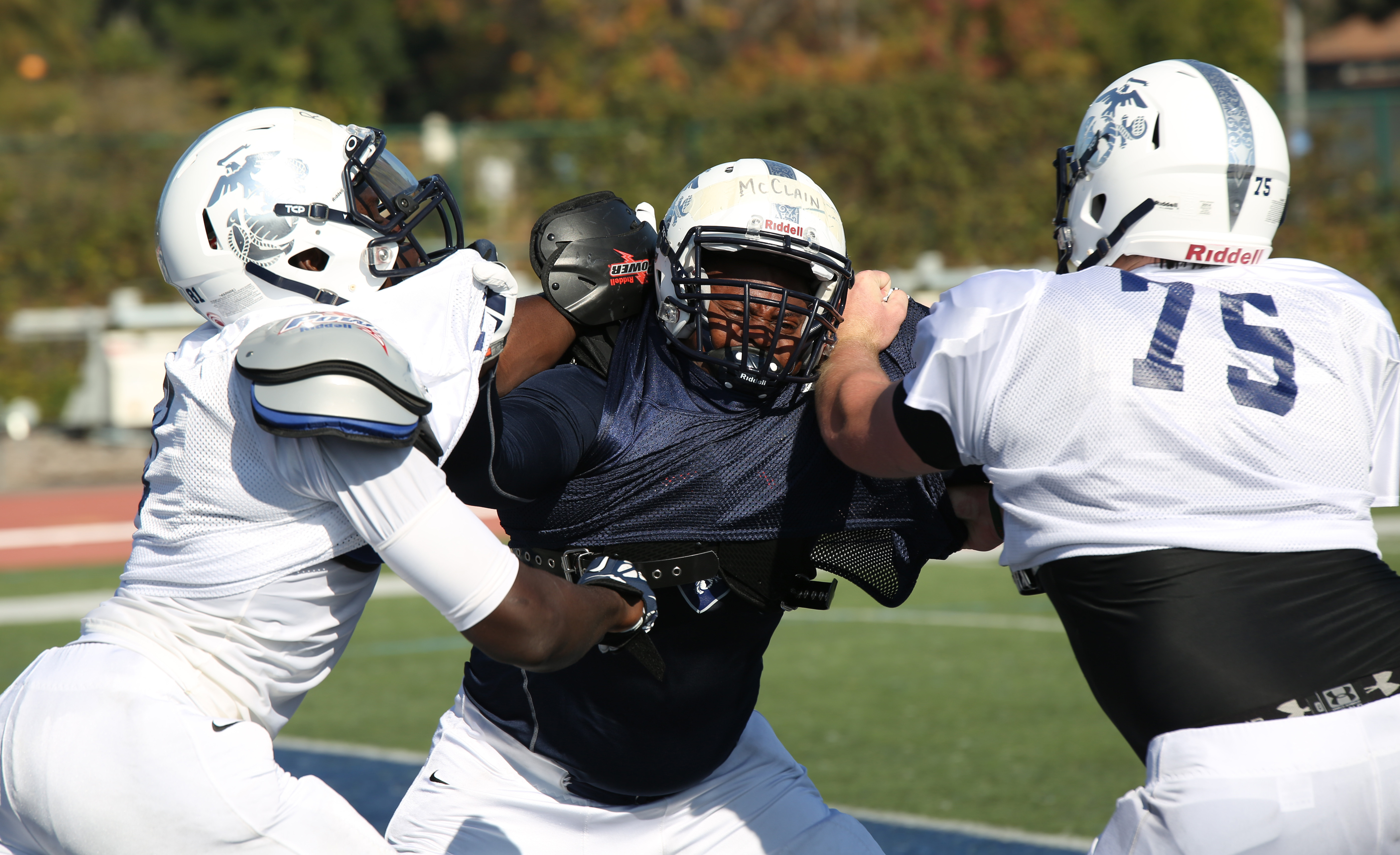 Football players in helmets and pads engaged in a blocking drill on a grass field.