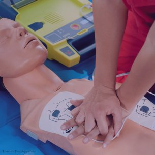Hands performing chest compressions on a CPR training mannequin with AED pads attached.