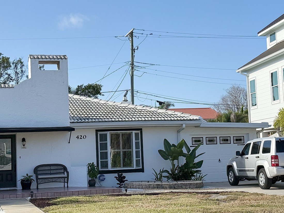 Overhead power lines and a utility pole above a white residential home with tropical landscaping.
