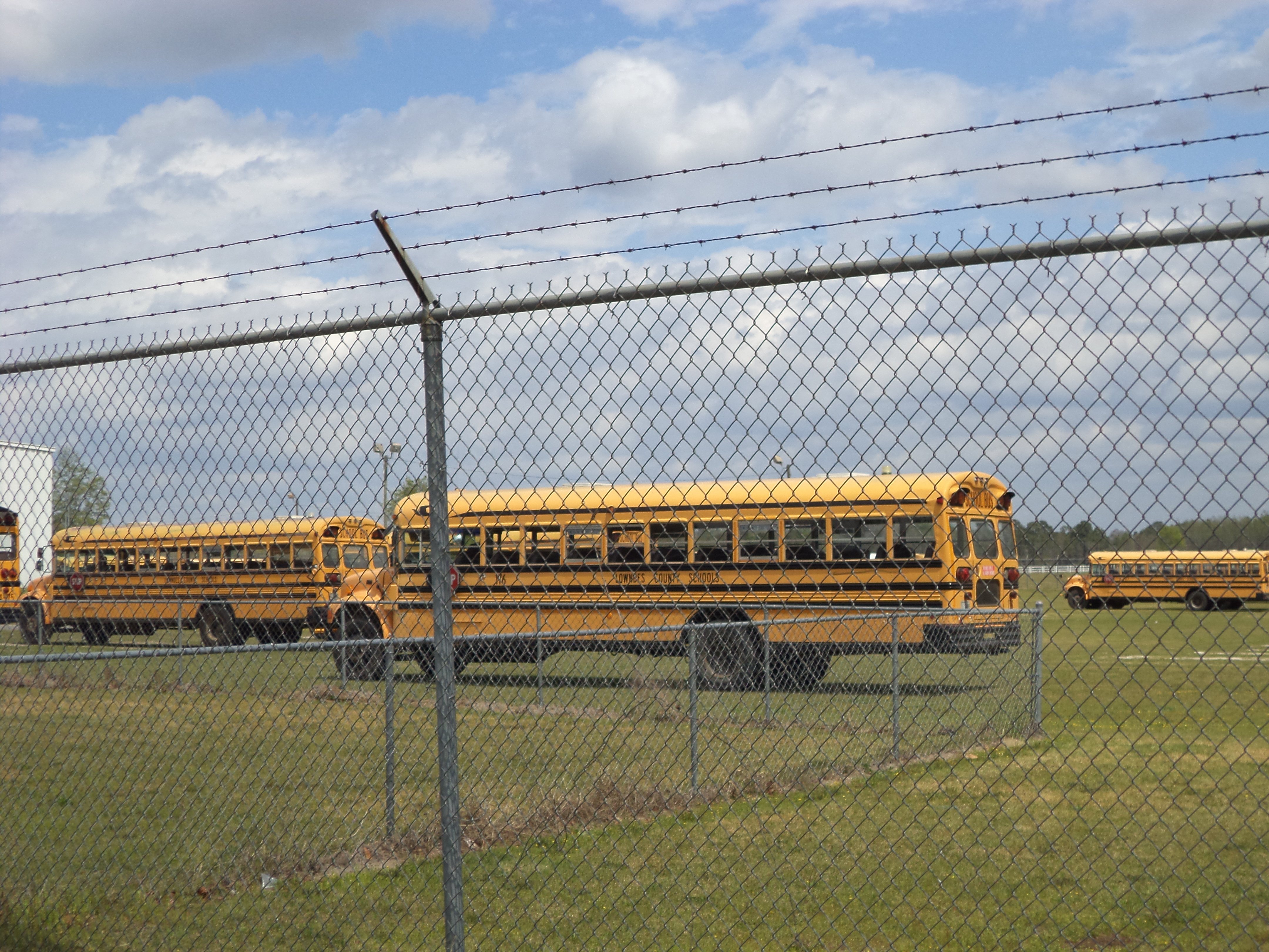 Yellow school buses parked in a fenced lot at a school district transportation yard.