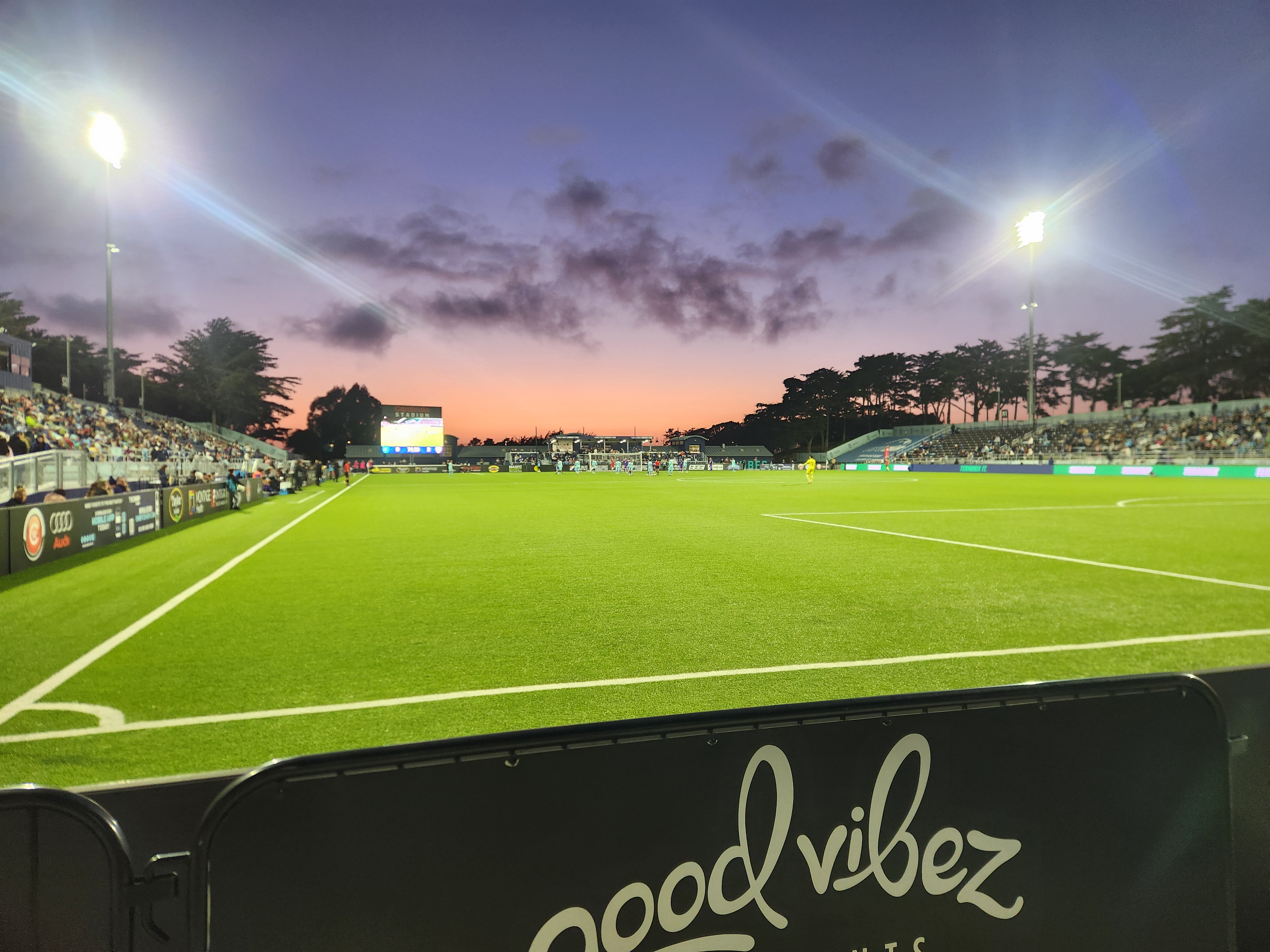 Soccer stadium lit up at dusk with fans in the stands and a pink sky.