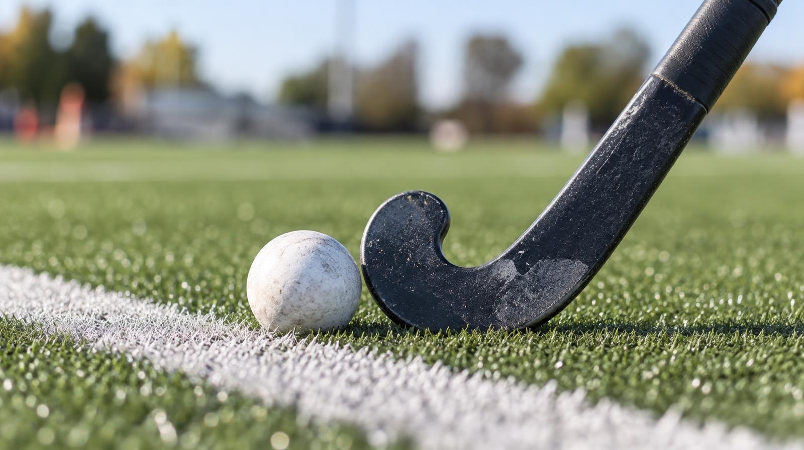A field hockey stick and ball resting on green artificial turf near a white line.