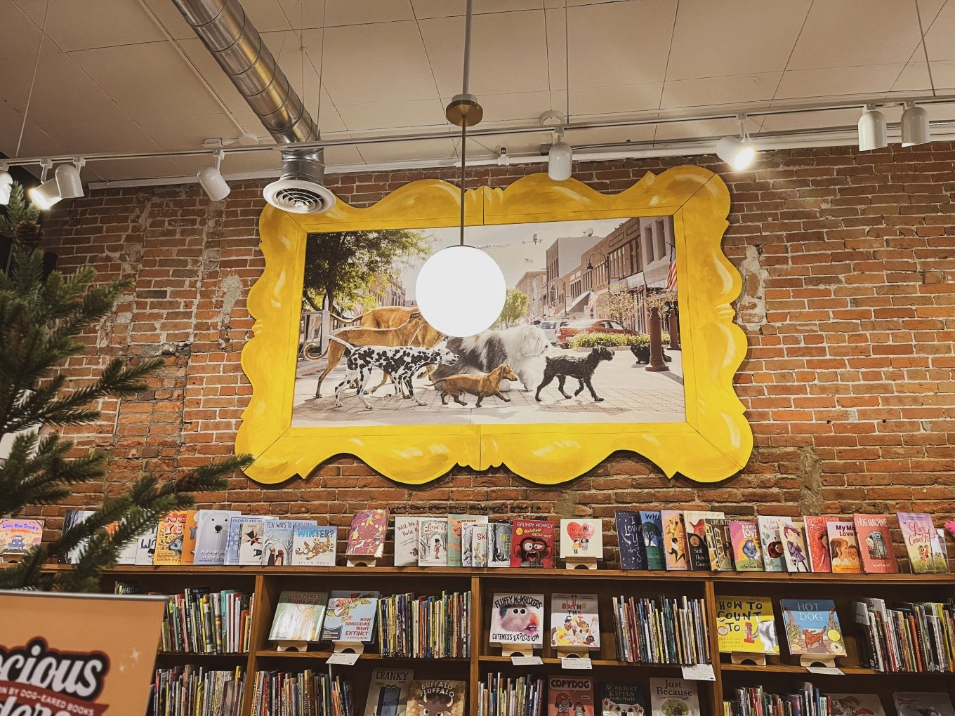Wooden bookshelves filled with books along a brick wall beneath a large ornate framed painting.