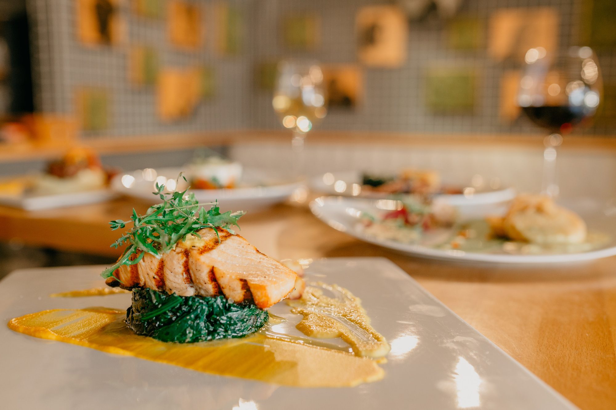 Tasty appetizing salmon fillet and green spinach decorated with arugula on plate with sauce on table in restaurant