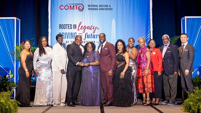 Group of people in formal attire posing on stage at a transportation conference.