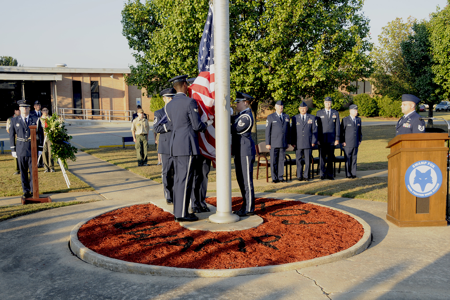 Honor guard members raise the American flag at a 9/11 anniversary ceremony with uniformed personnel nearby.