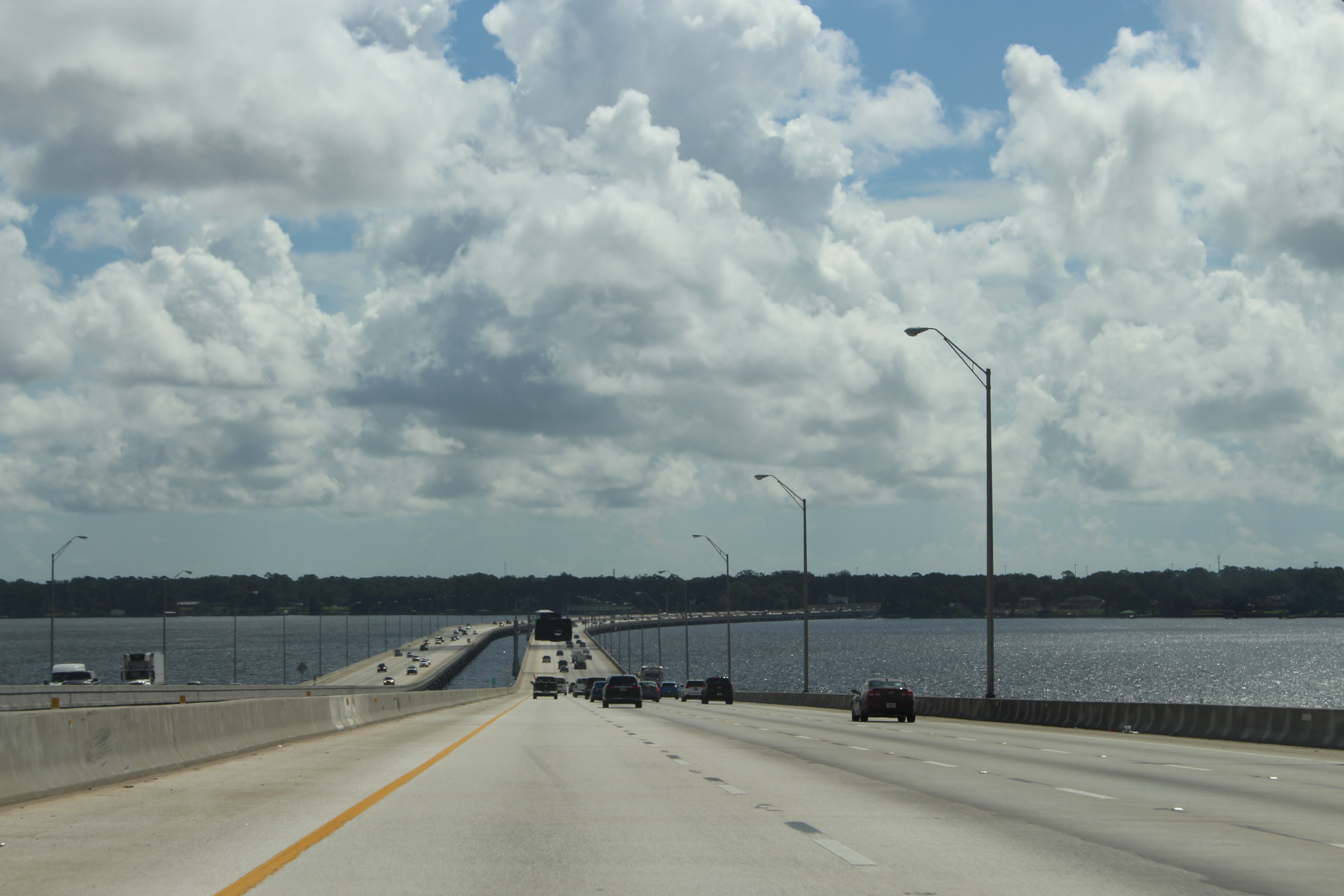 Multi-lane highway bridge over water with vehicles and light poles under a partly cloudy sky.