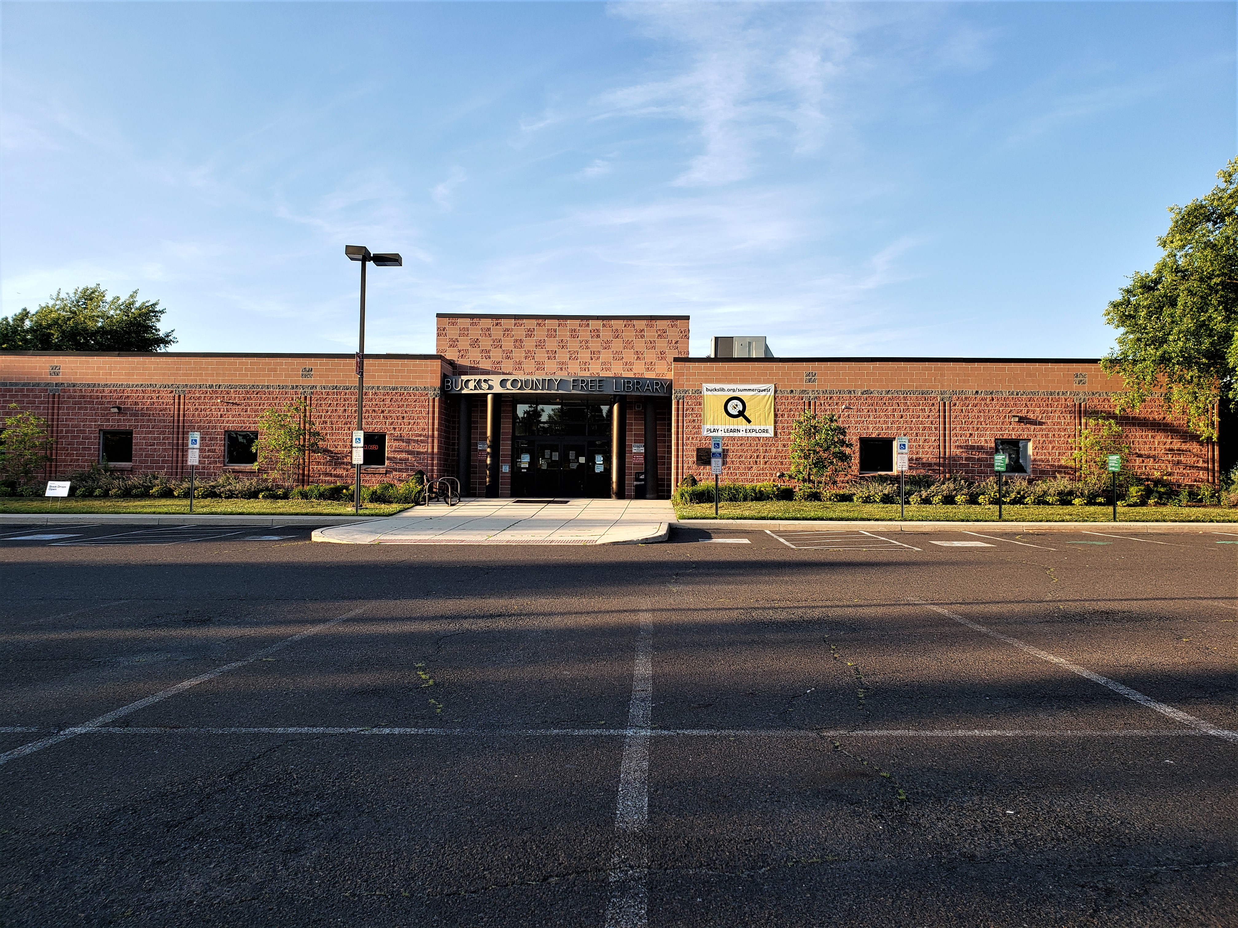 Single-story red brick library building with a parking lot and trees out front.