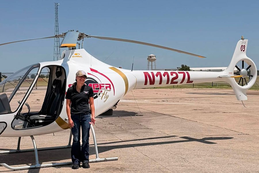 Person standing next to a white helicopter with red and gold Semper Fly markings on a paved airfield.