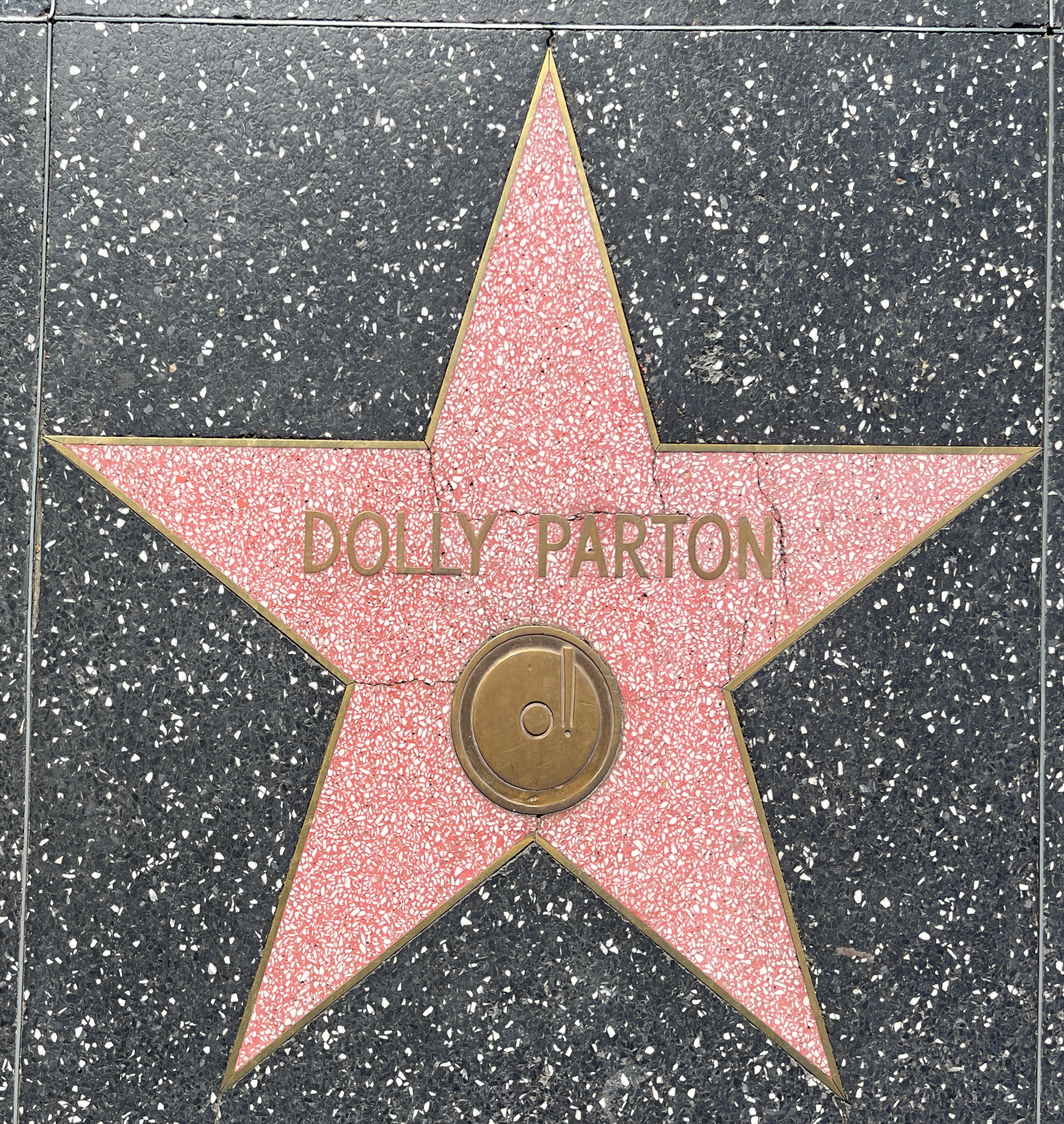 Pink terrazzo star with gold lettering reading Dolly Parton set in dark granite sidewalk.