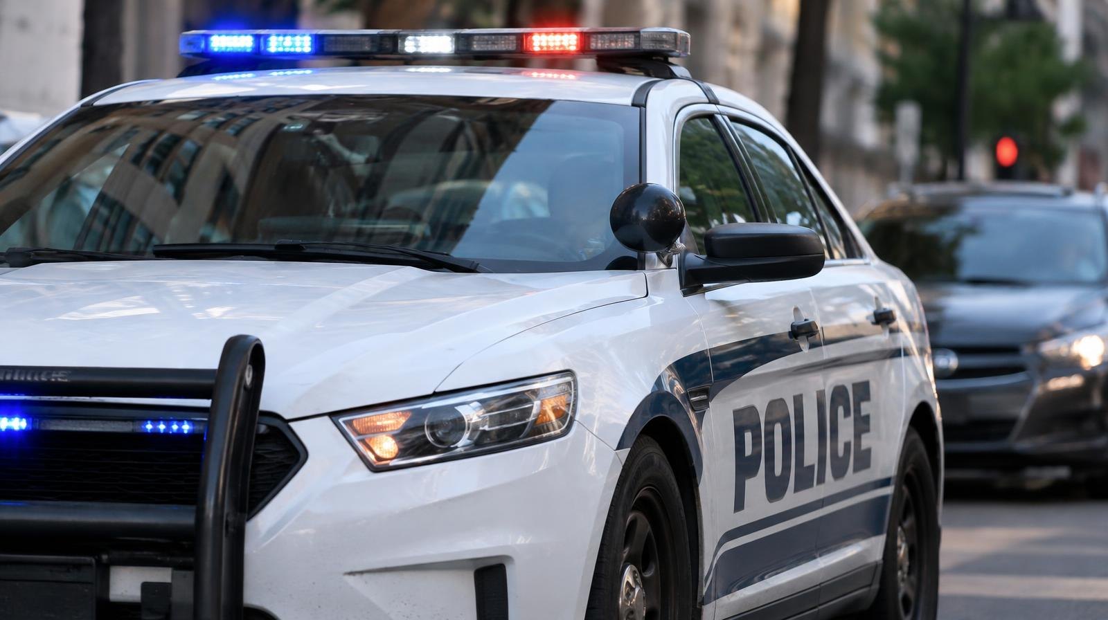 A police patrol car with red and blue emergency lights on, parked on an urban street.