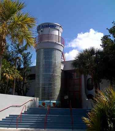 Exterior entrance of MAST Academy with a glass-block tower and palm trees.