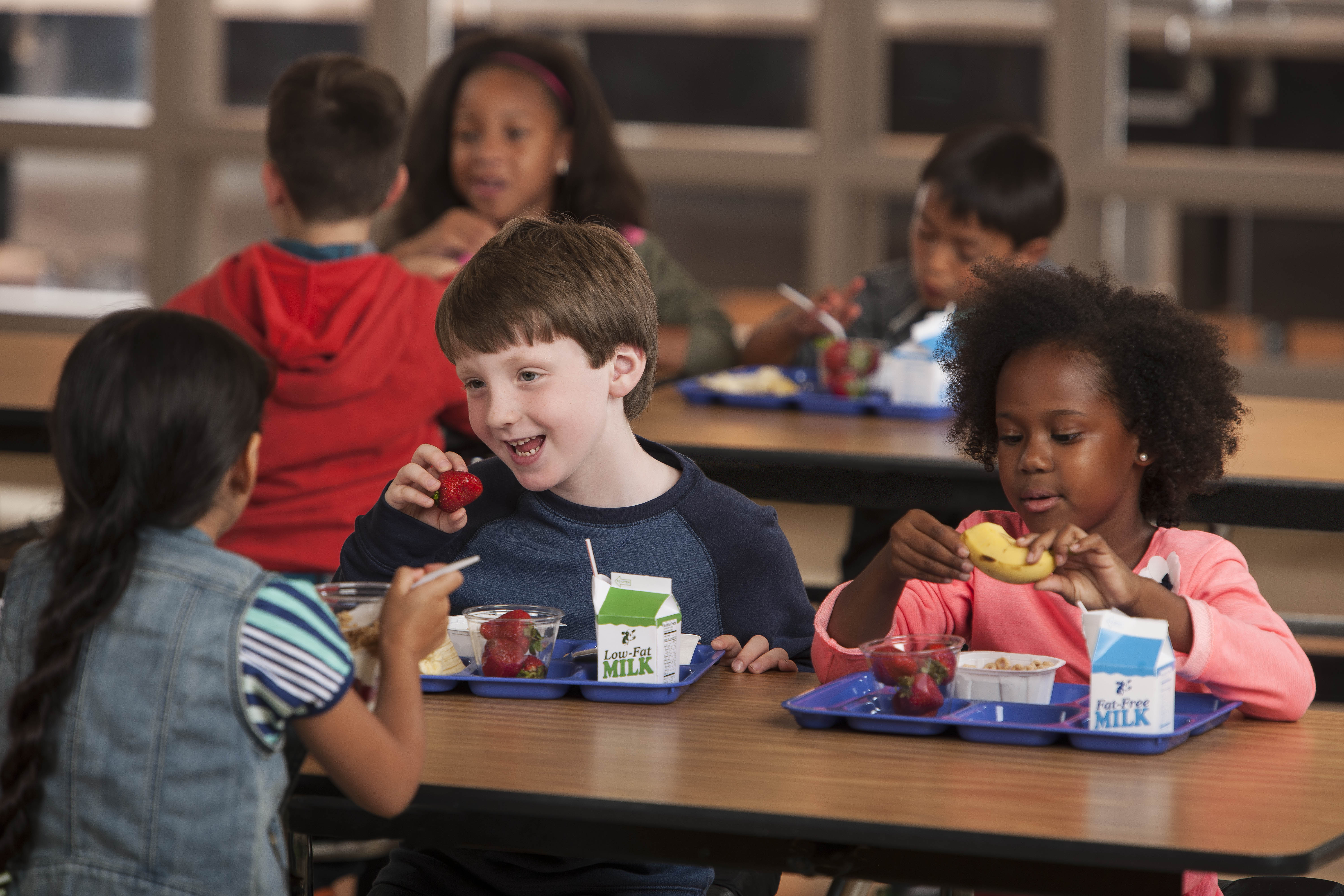 Young children eating breakfast at a school cafeteria table with milk cartons.