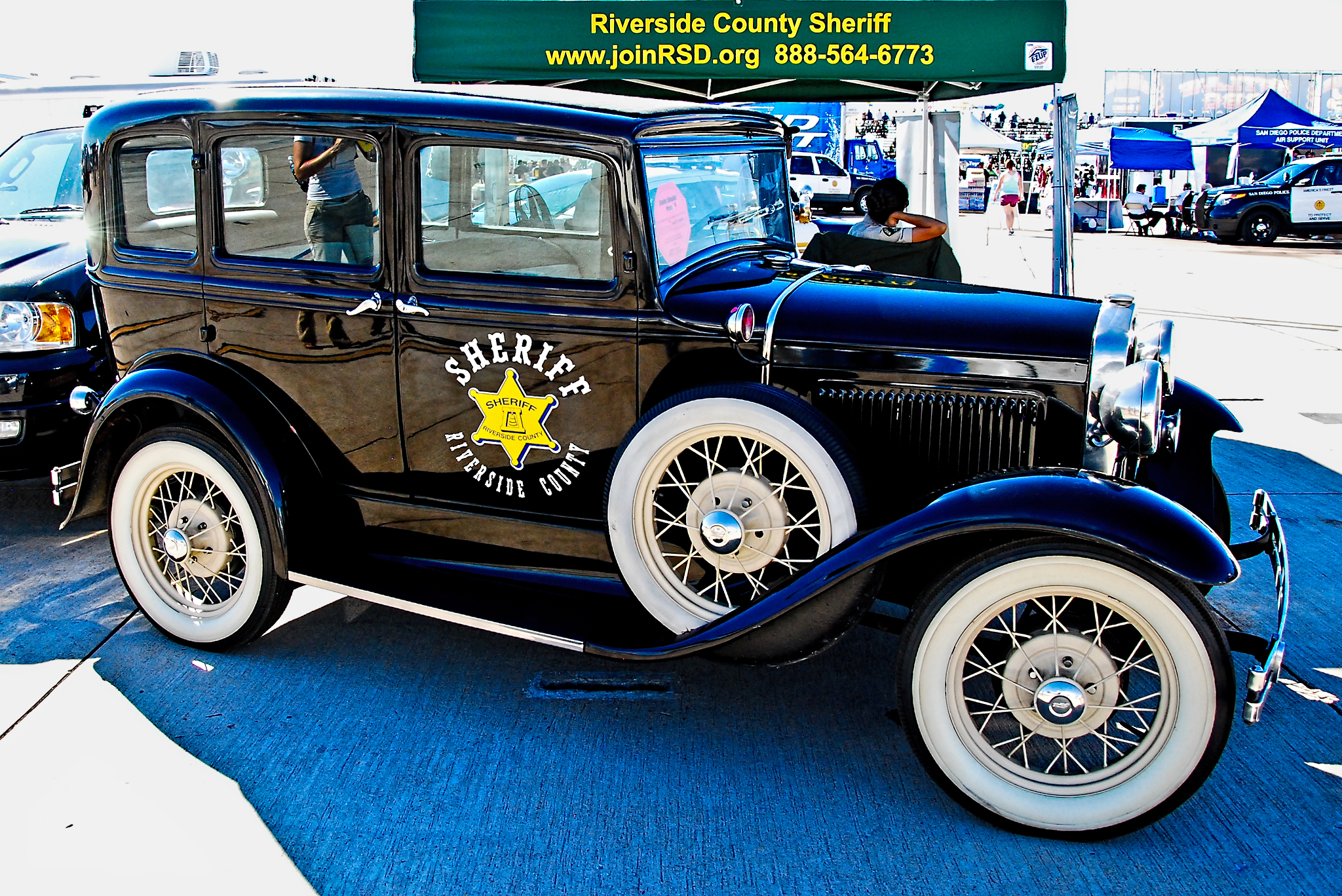 Vintage black sedan with Sheriff markings and gold star badge on display at a public event.
