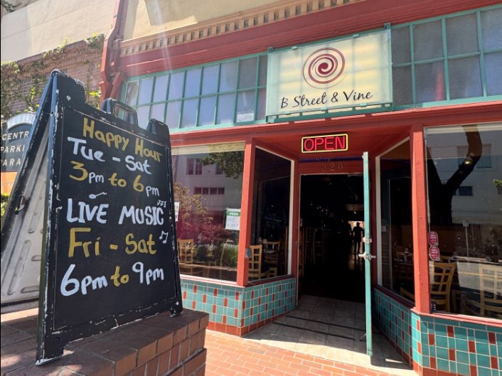 Storefront of a wine bar with a chalkboard sign advertising live music and happy hour.