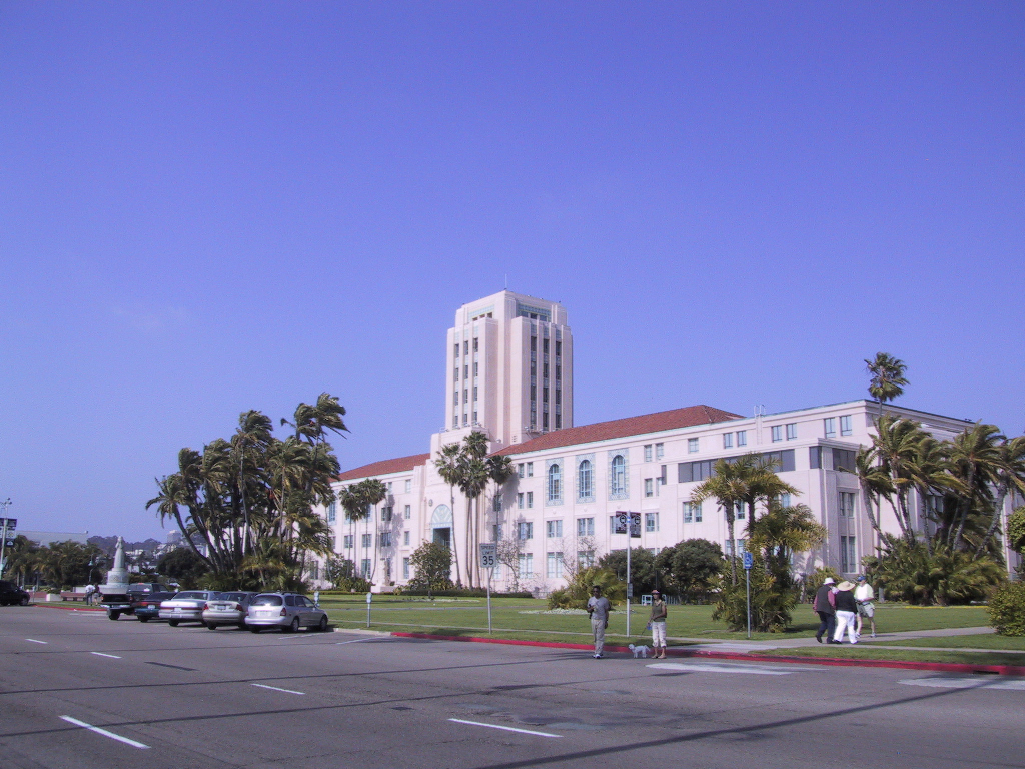 White Art Deco government building with central tower and palm trees under blue sky.