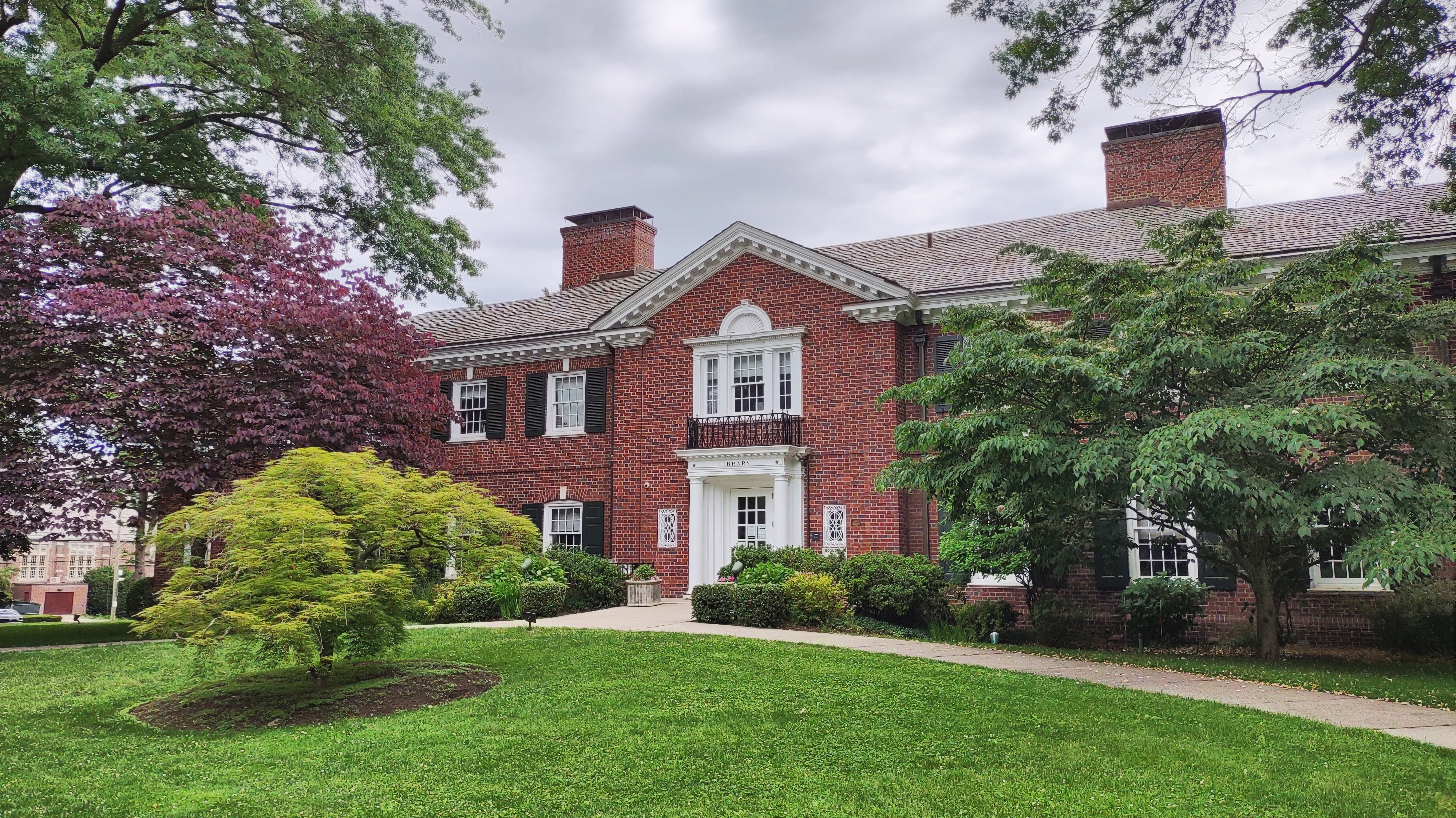Red brick colonial-style Bronxville Public Library building with white trim, surrounded by mature trees and a green lawn.