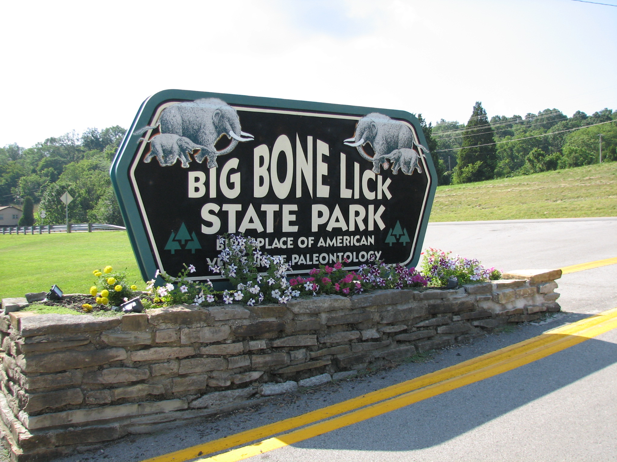 Stone park entrance sign flanked by mammoth sculptures and colorful flowers