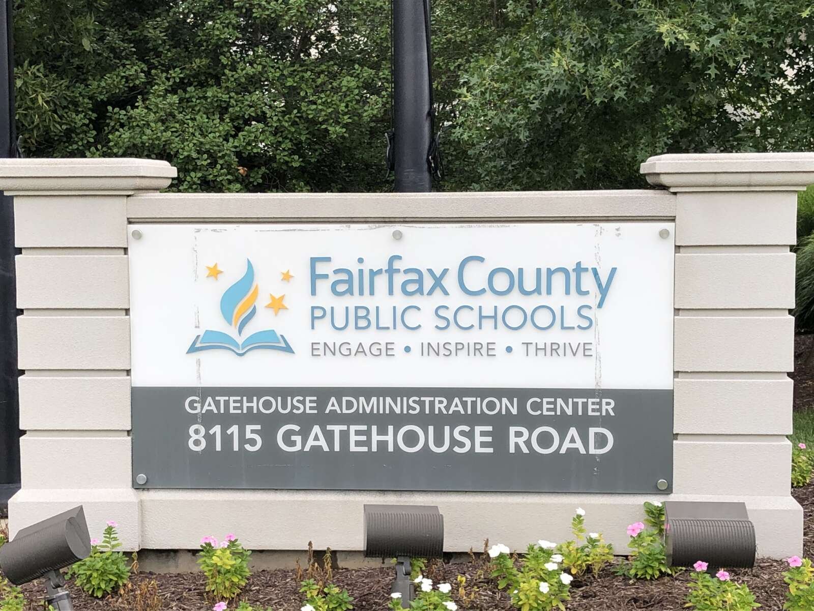 Stone monument sign for Fairfax County Public Schools Gatehouse Administration Center surrounded by trees and flowers.