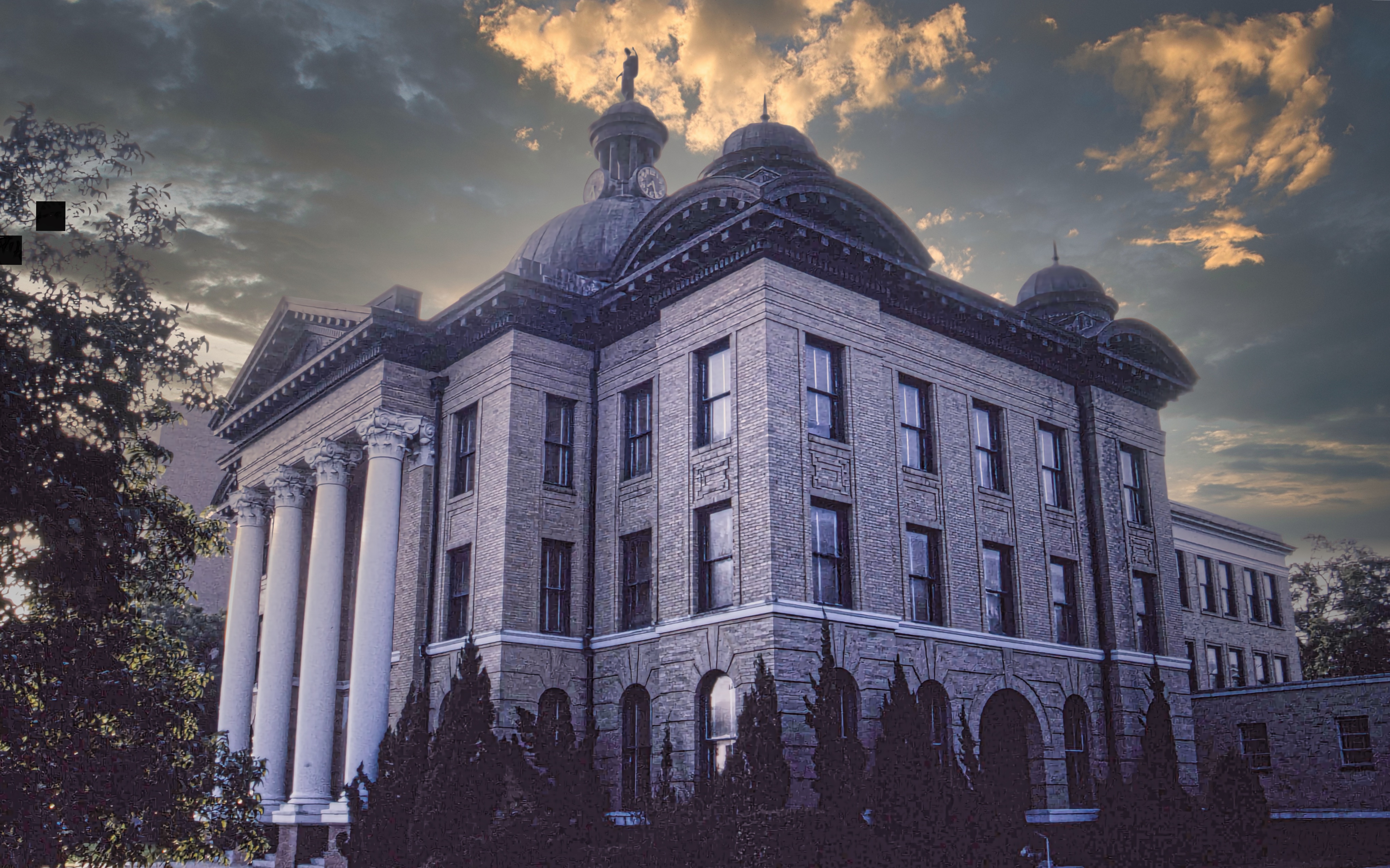 Historic domed stone courthouse with classical columns under a dramatic cloudy sky.