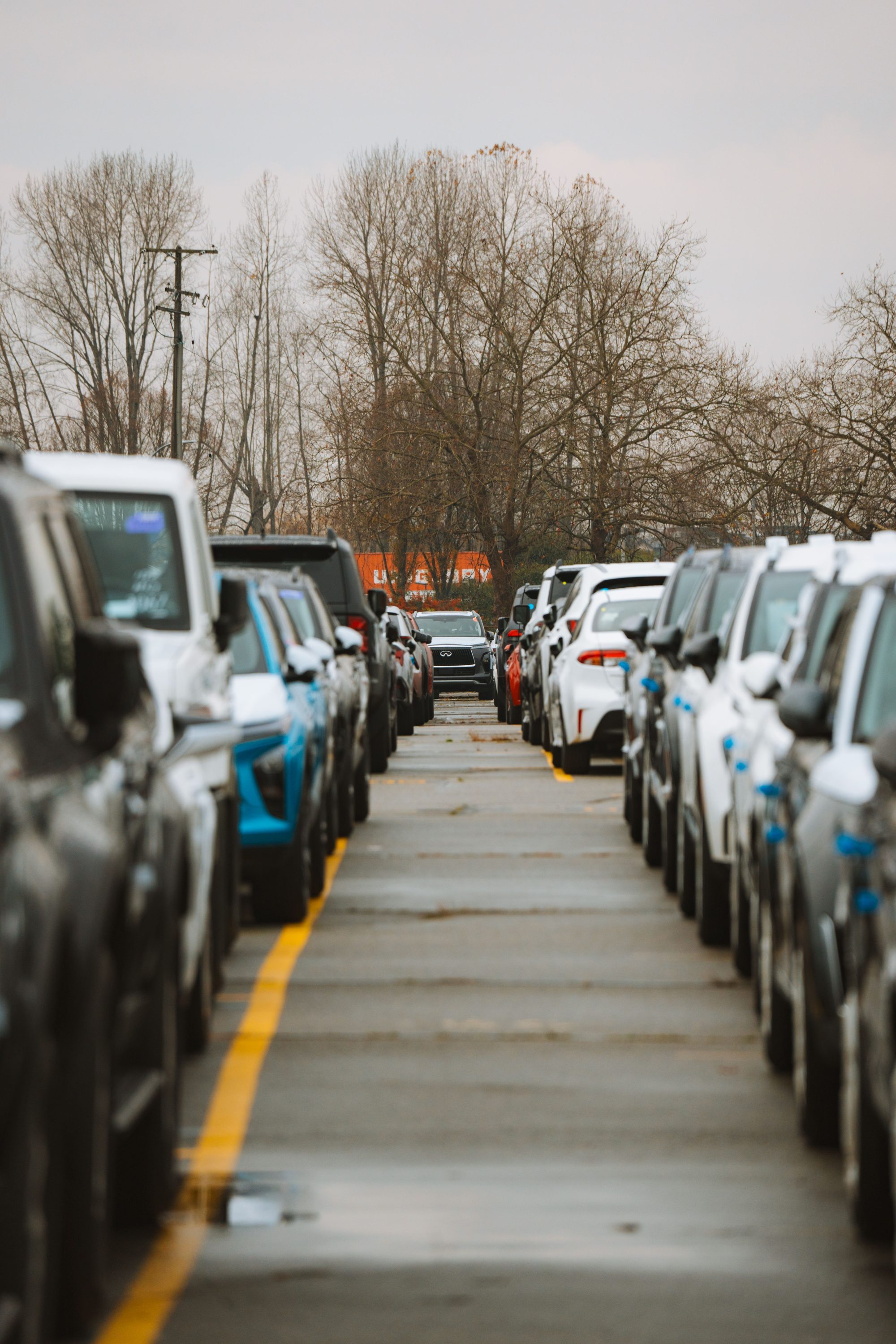 A perspective view of parked cars lined neatly on a wet road under an overcast sky.