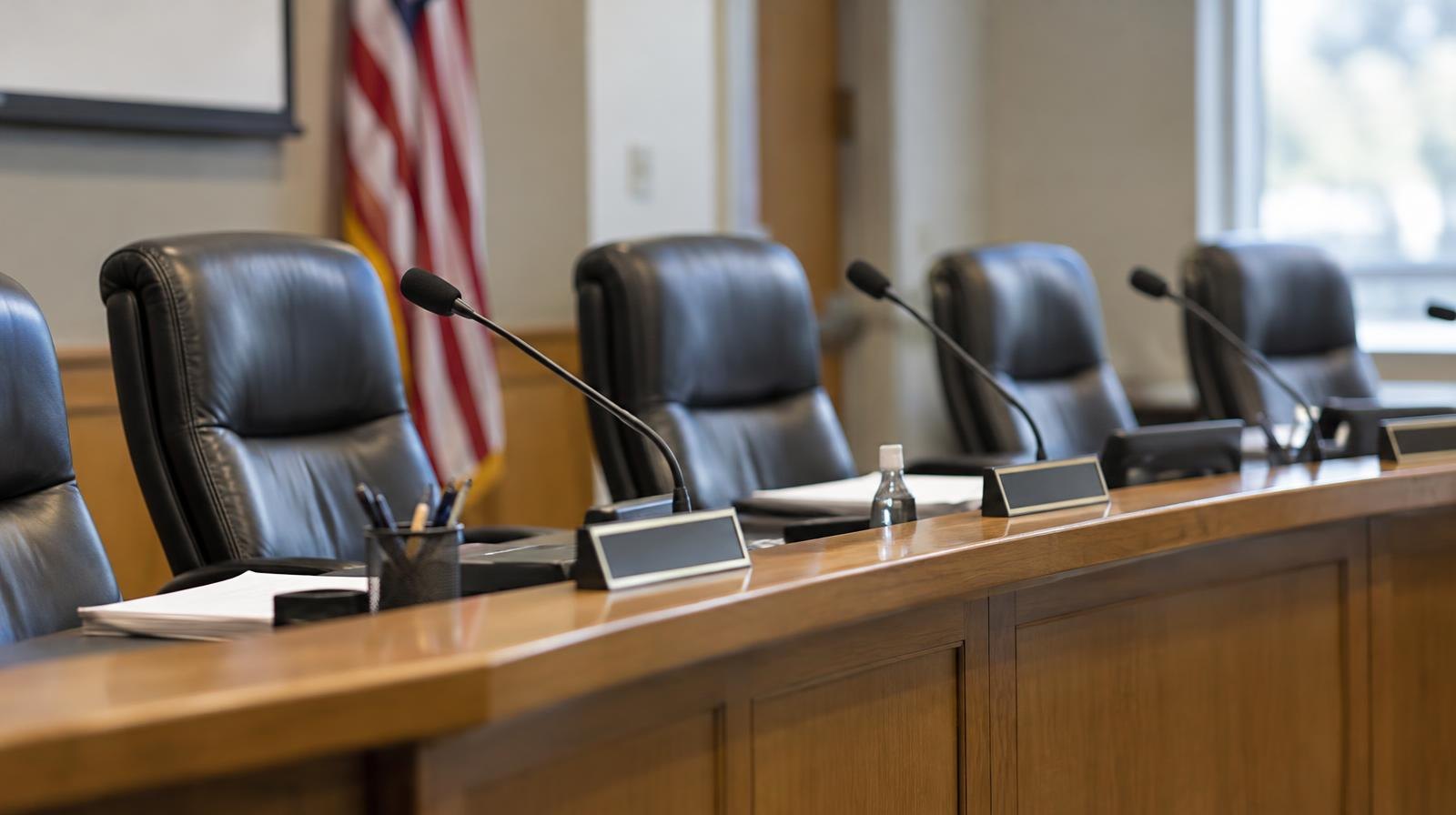 Empty curved dais with name placards and microphones in a meeting room.