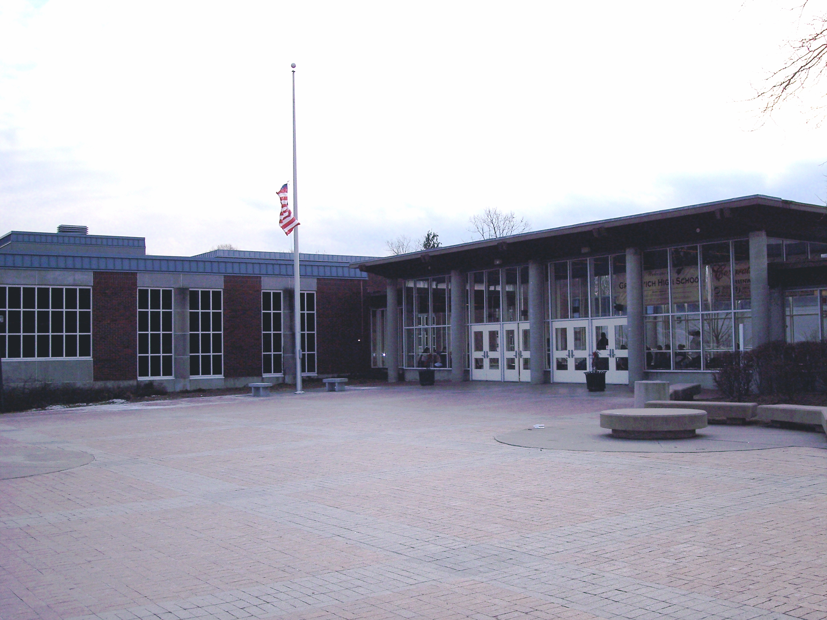 Brick exterior of a high school building with glass entrance canopy and flagpole.