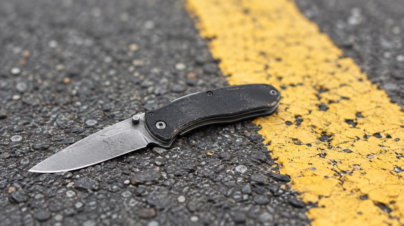 A folding pocket knife lying on asphalt next to a yellow road marking.