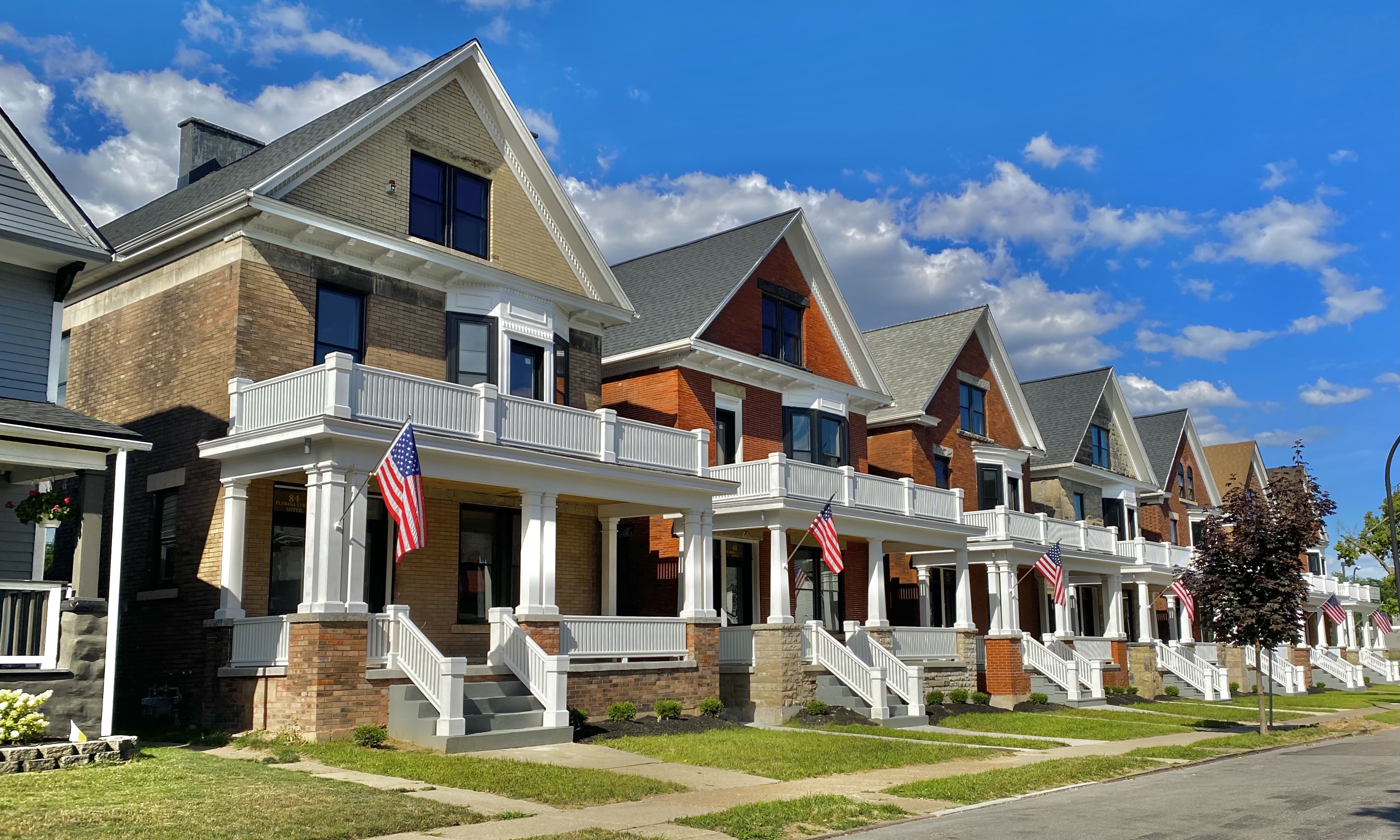 A row of similar brick rowhouses with white-columned porches lining a residential street.