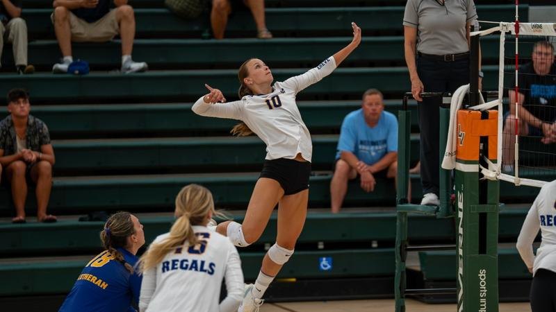 A volleyball player in a white uniform jumps to spike the ball at the net.