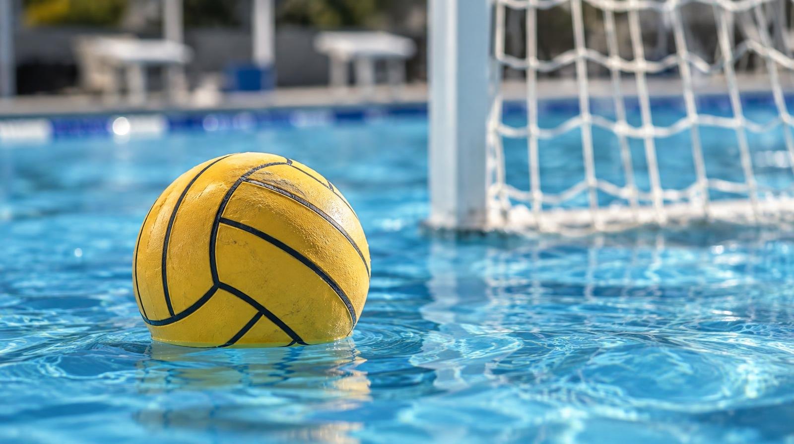 A water polo ball floating on the surface of a bright blue pool near a white goal net.