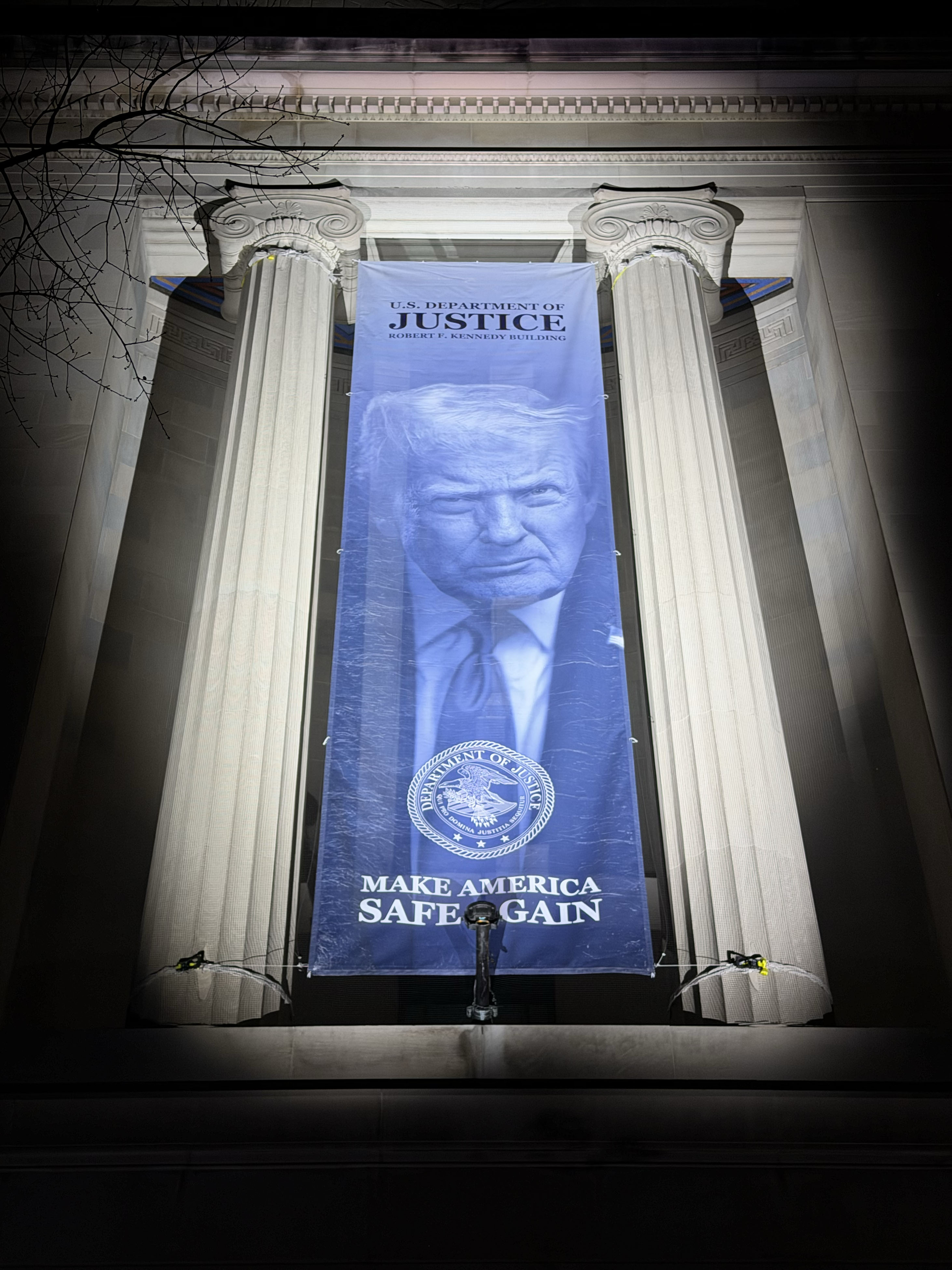 A large banner on the Department of Justice building facade, photographed at night.