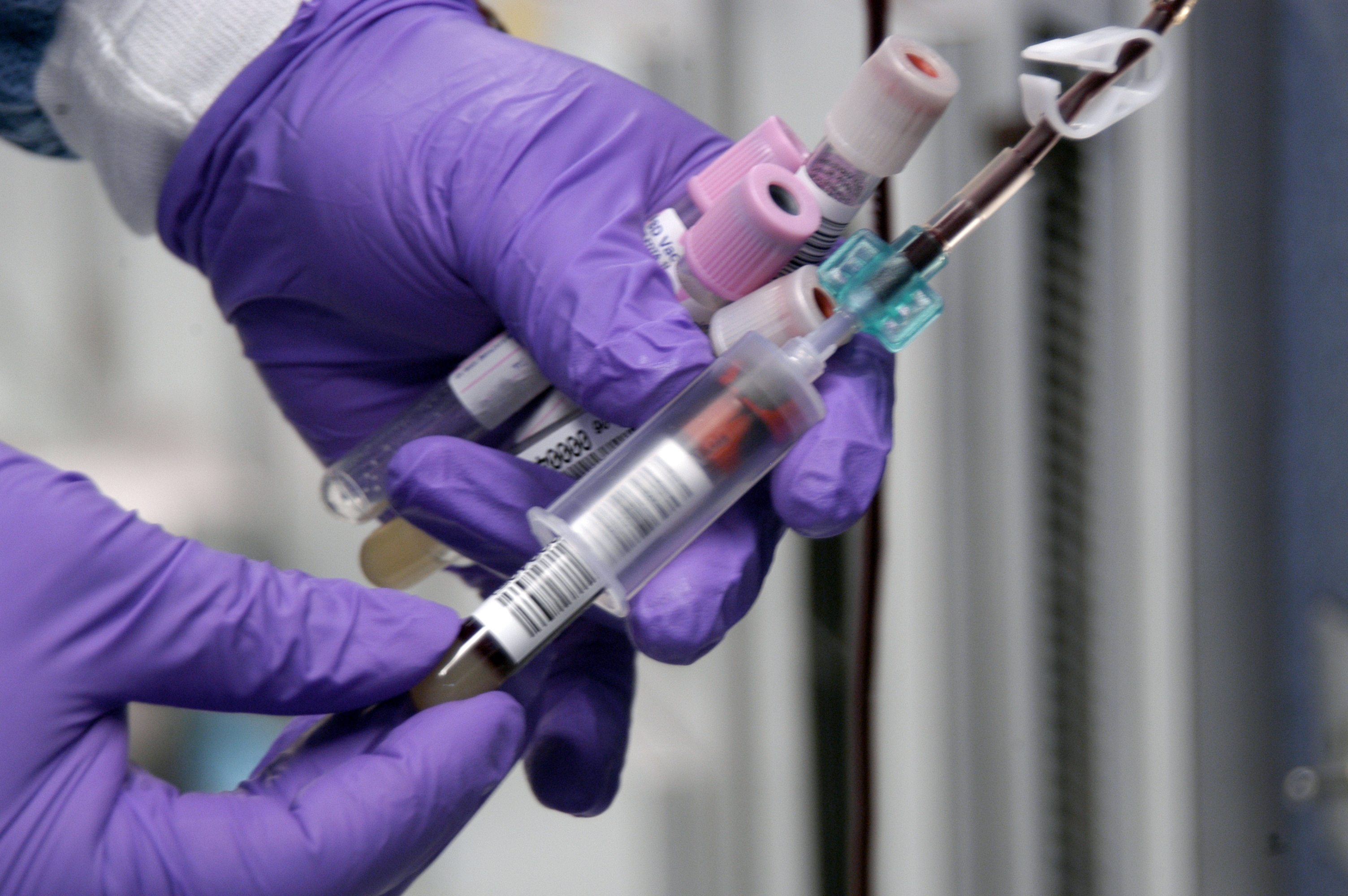 A medical worker in gloves takes blood samples from a seated donor's arm.