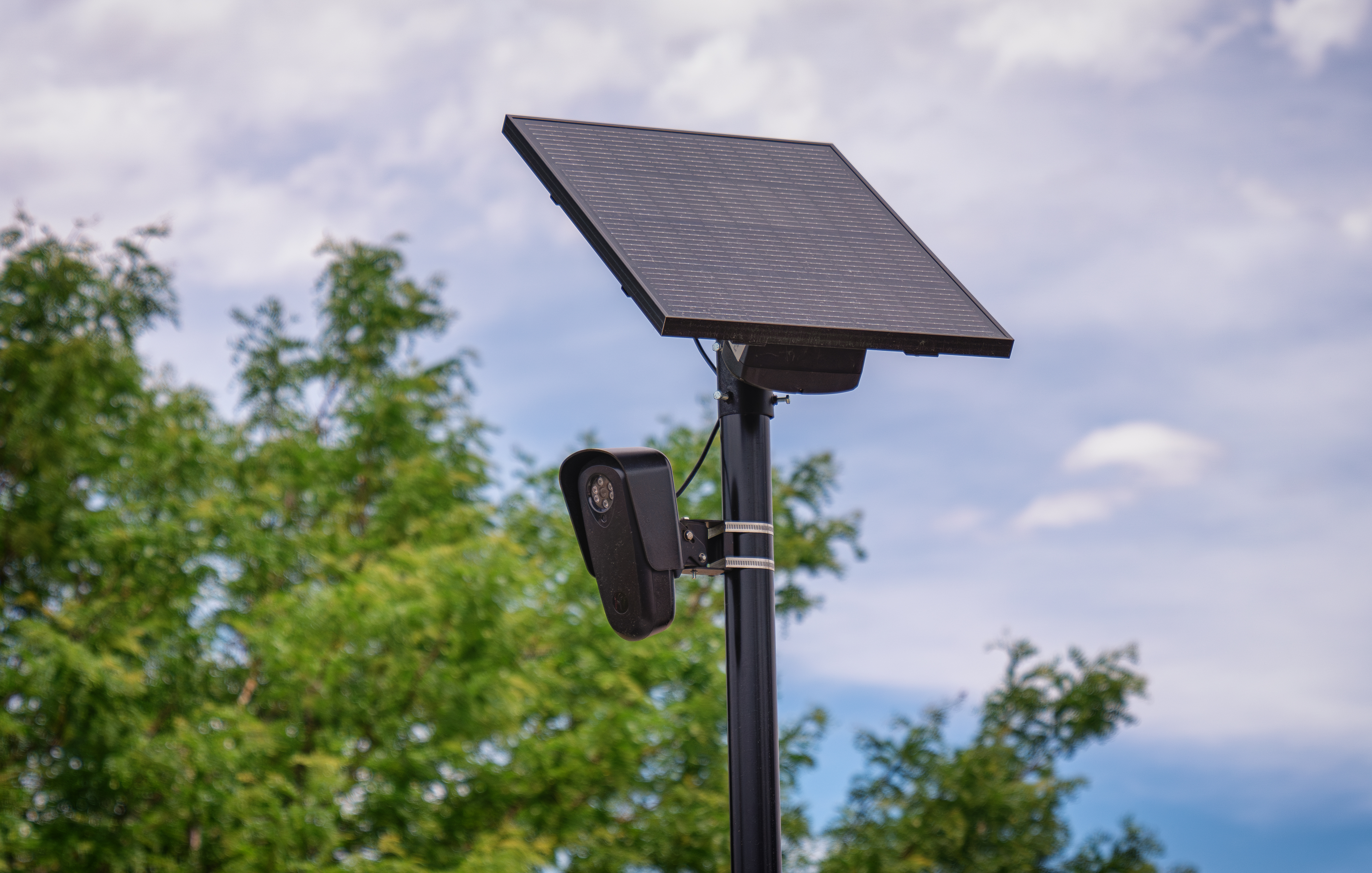 Flock Safety ALPR camera with solar panel mounted on a black pole outdoors.
