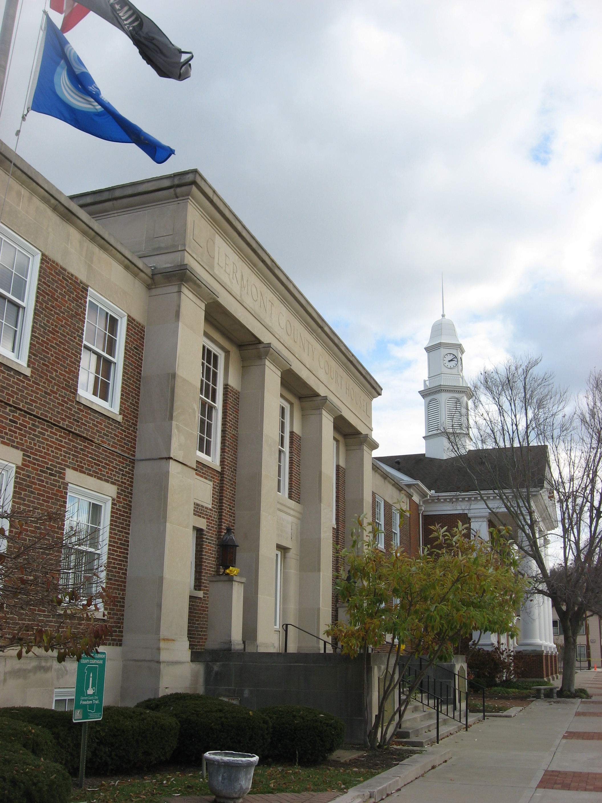 Brick government building with stone columns, flags, and a white clock tower.