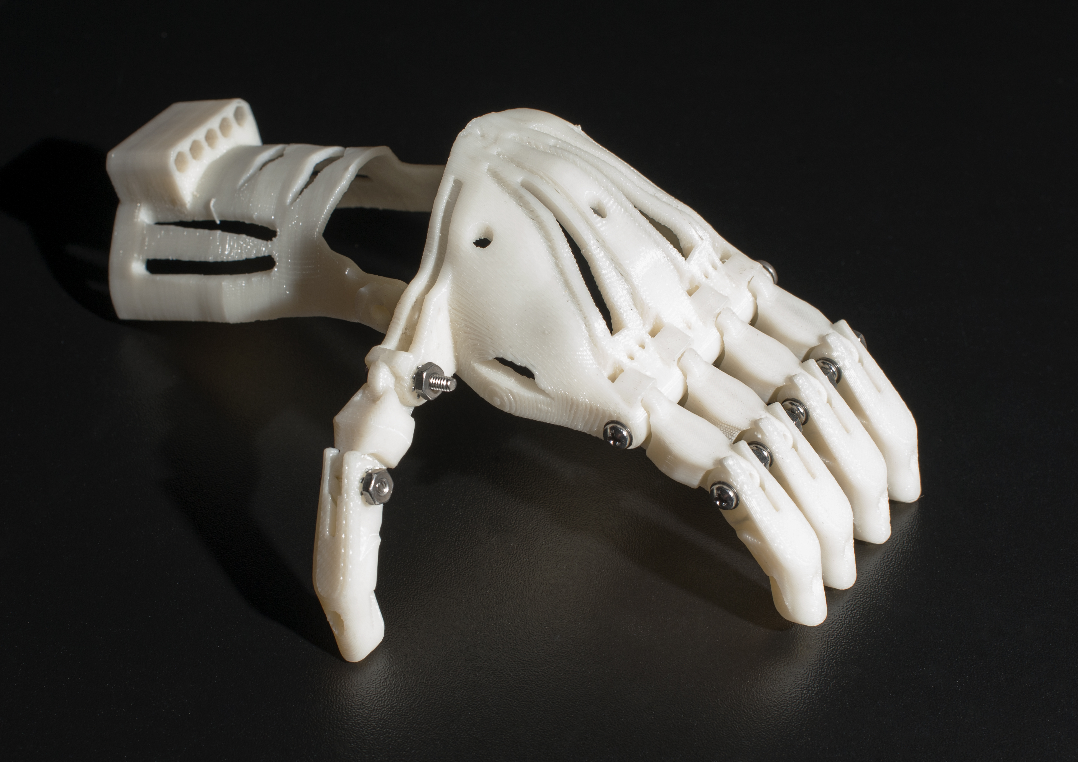 White 3D-printed prosthetic hand with articulated fingers and metal screws at the joints.