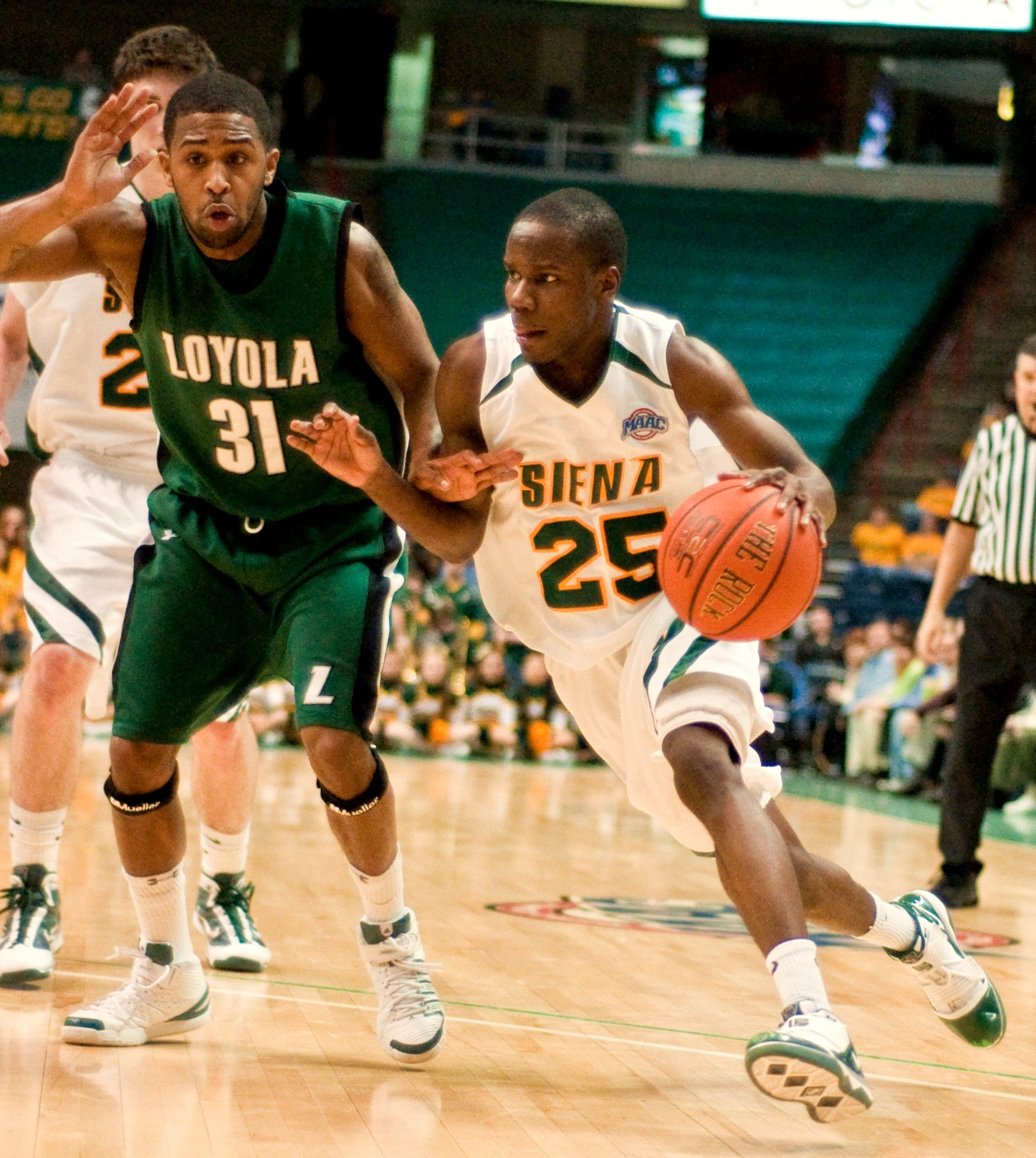A Siena Saints basketball player dribbling toward the basket during a home game.