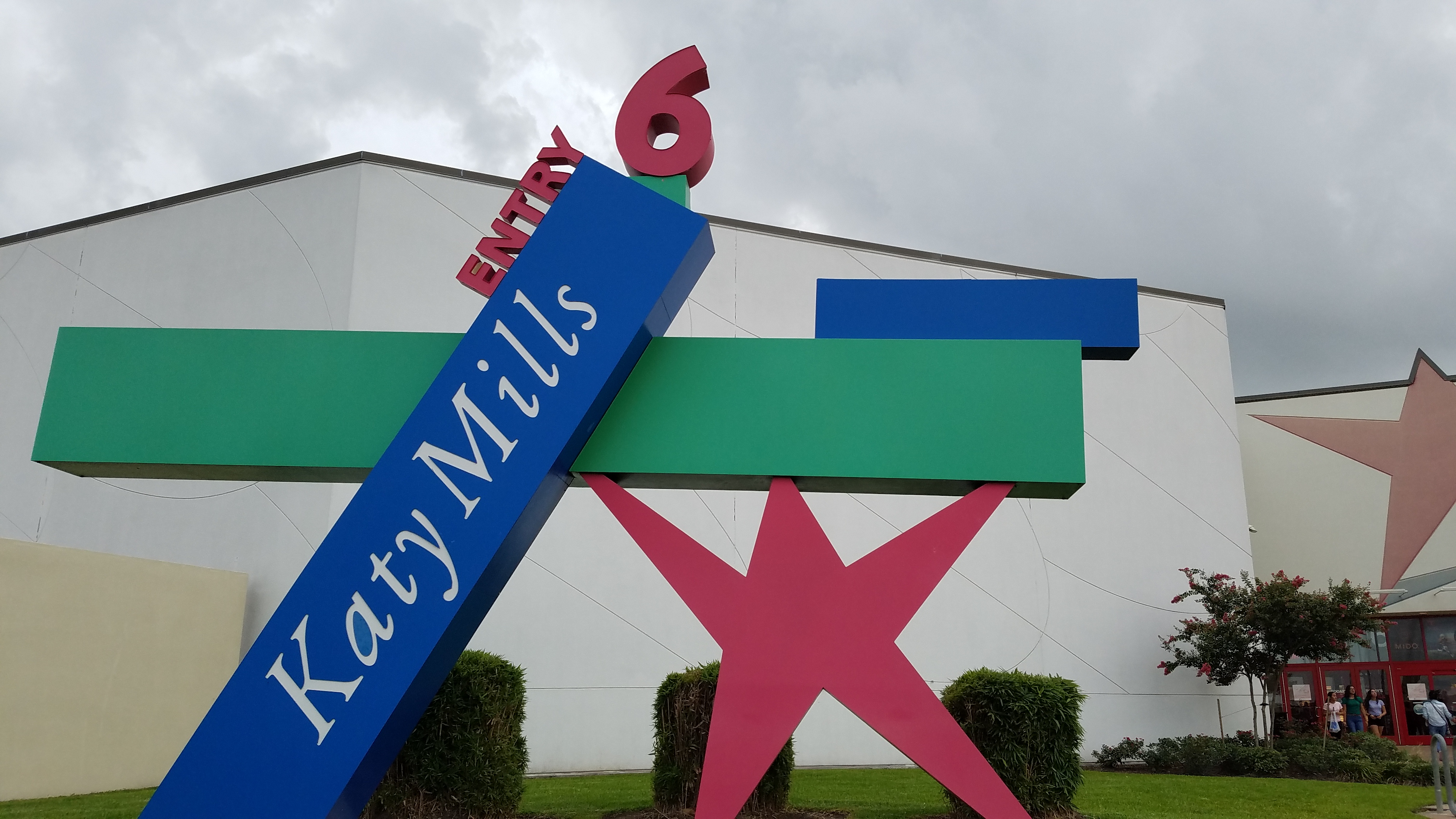Colorful Katy Mills mall entrance sign with a large pink star and teal panels against an overcast sky.