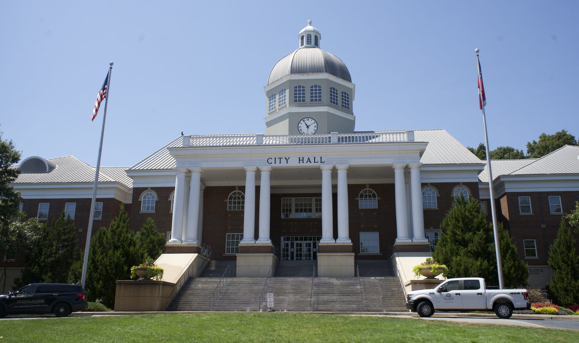 Red-brick city hall building with white columns and a domed clock tower on a sunny day.