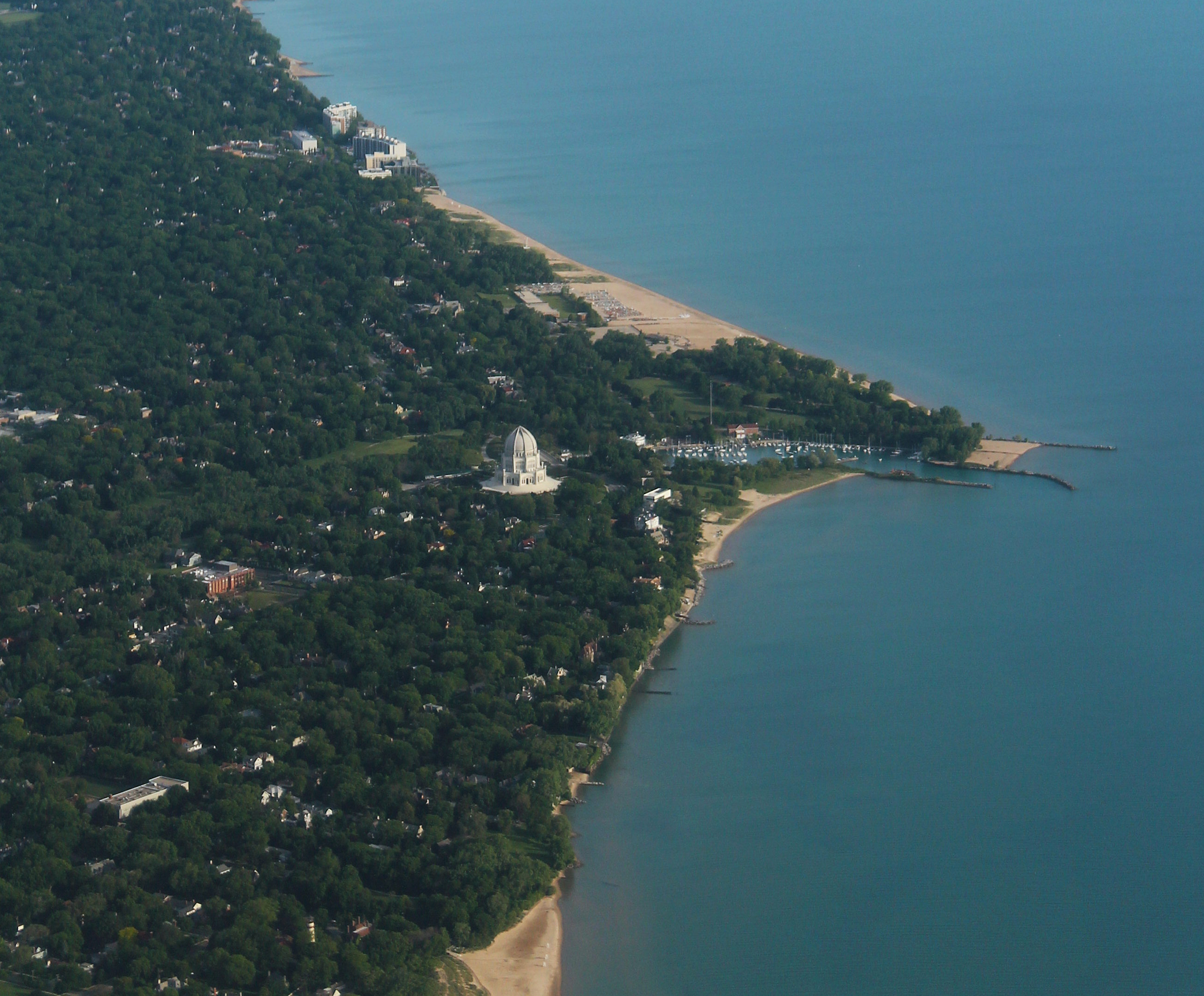 Aerial view of a lakefront park with a sandy beach, pier, and tree canopy.