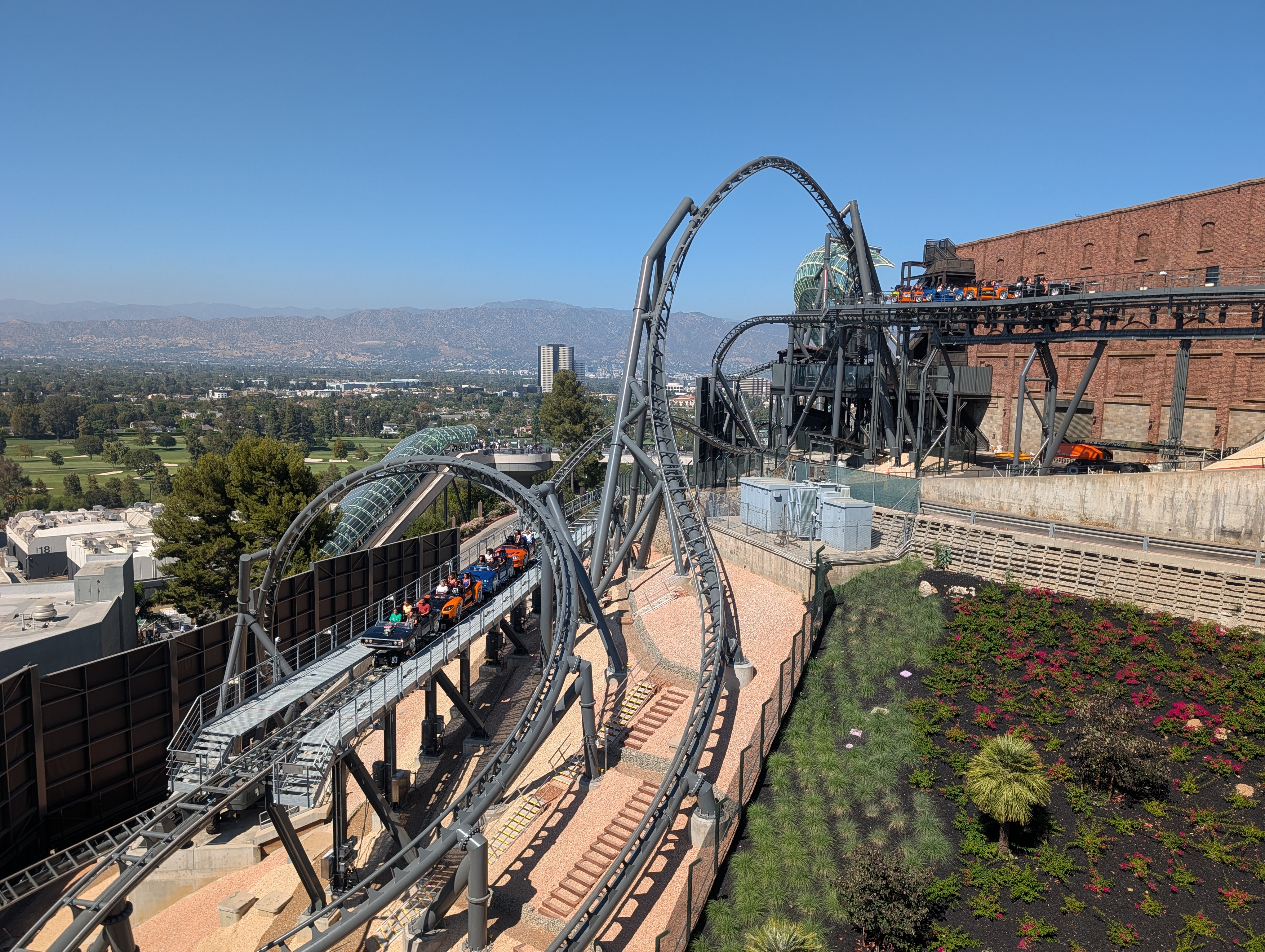 Outdoor steel roller coaster with loop and glass enclosure section, mountains visible behind.