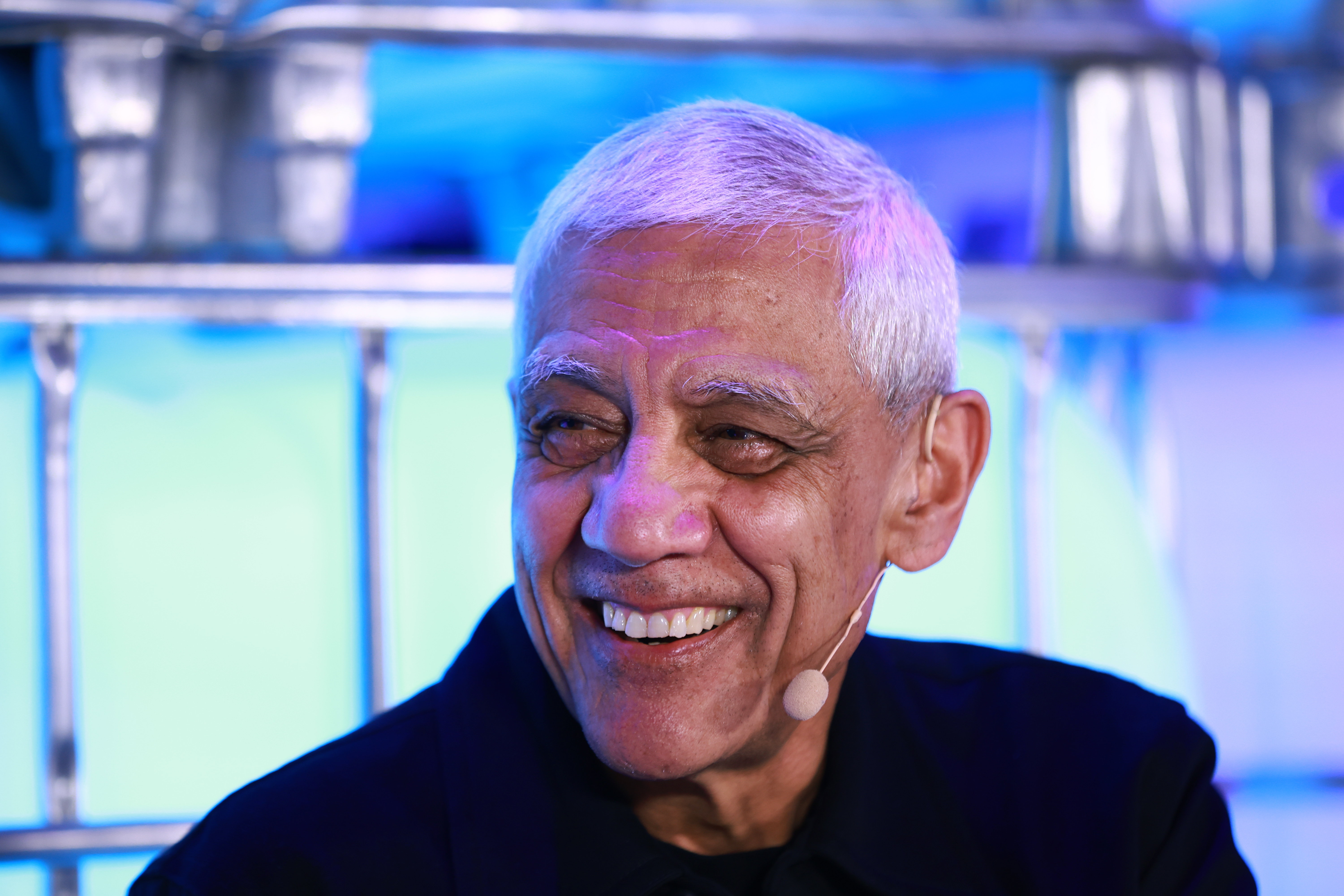 Older man with gray hair smiling broadly against a blue-lit background.