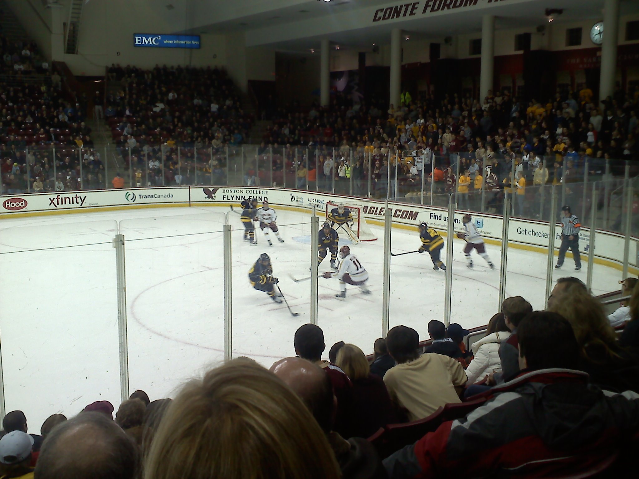 College ice hockey players compete on the ice in a packed indoor arena.