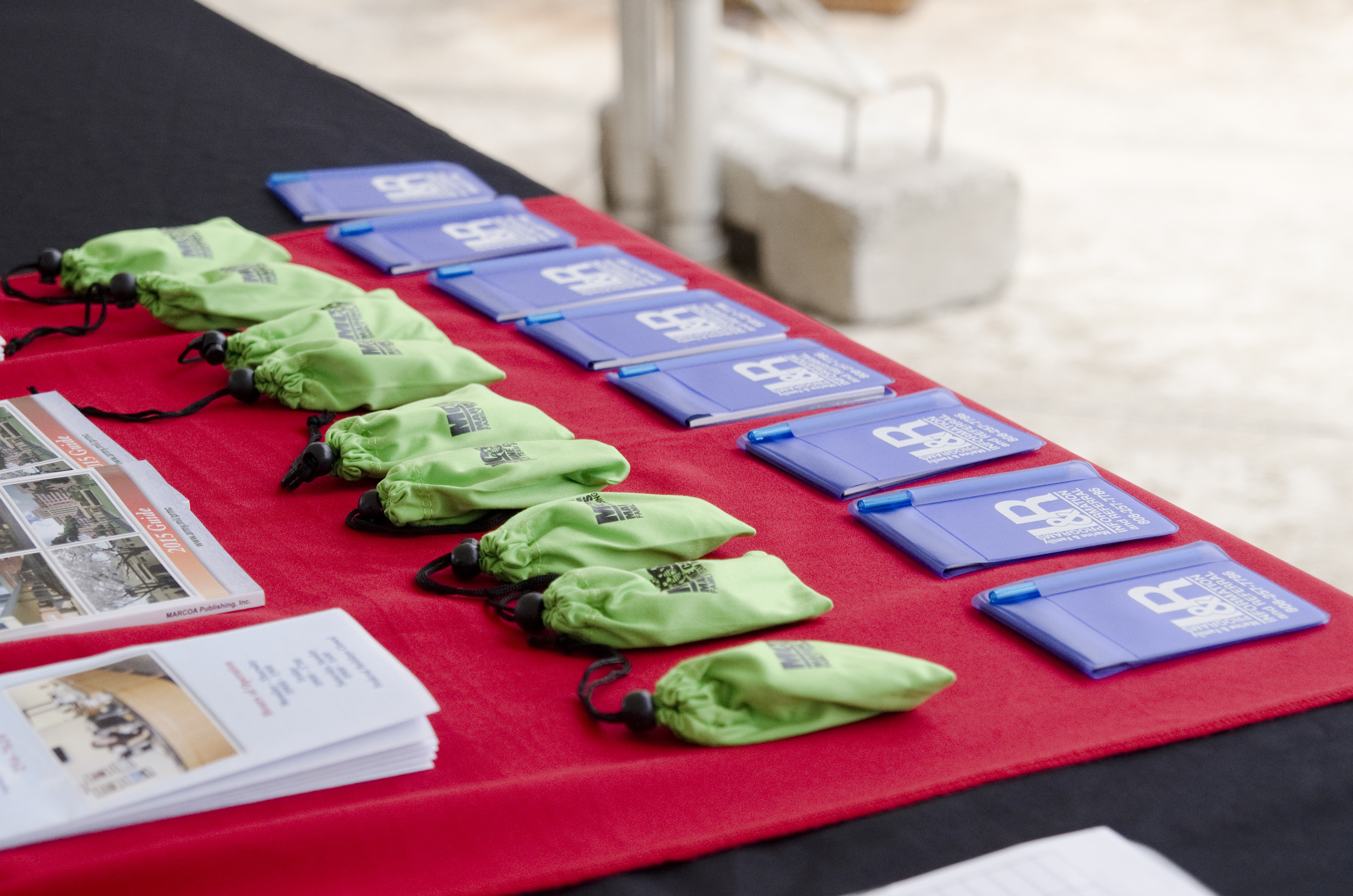 A red-draped table with rows of blue booklets and green drawstring bags.