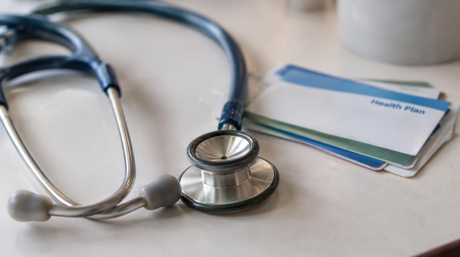 A stethoscope resting beside a small stack of medical insurance cards on a plain surface.