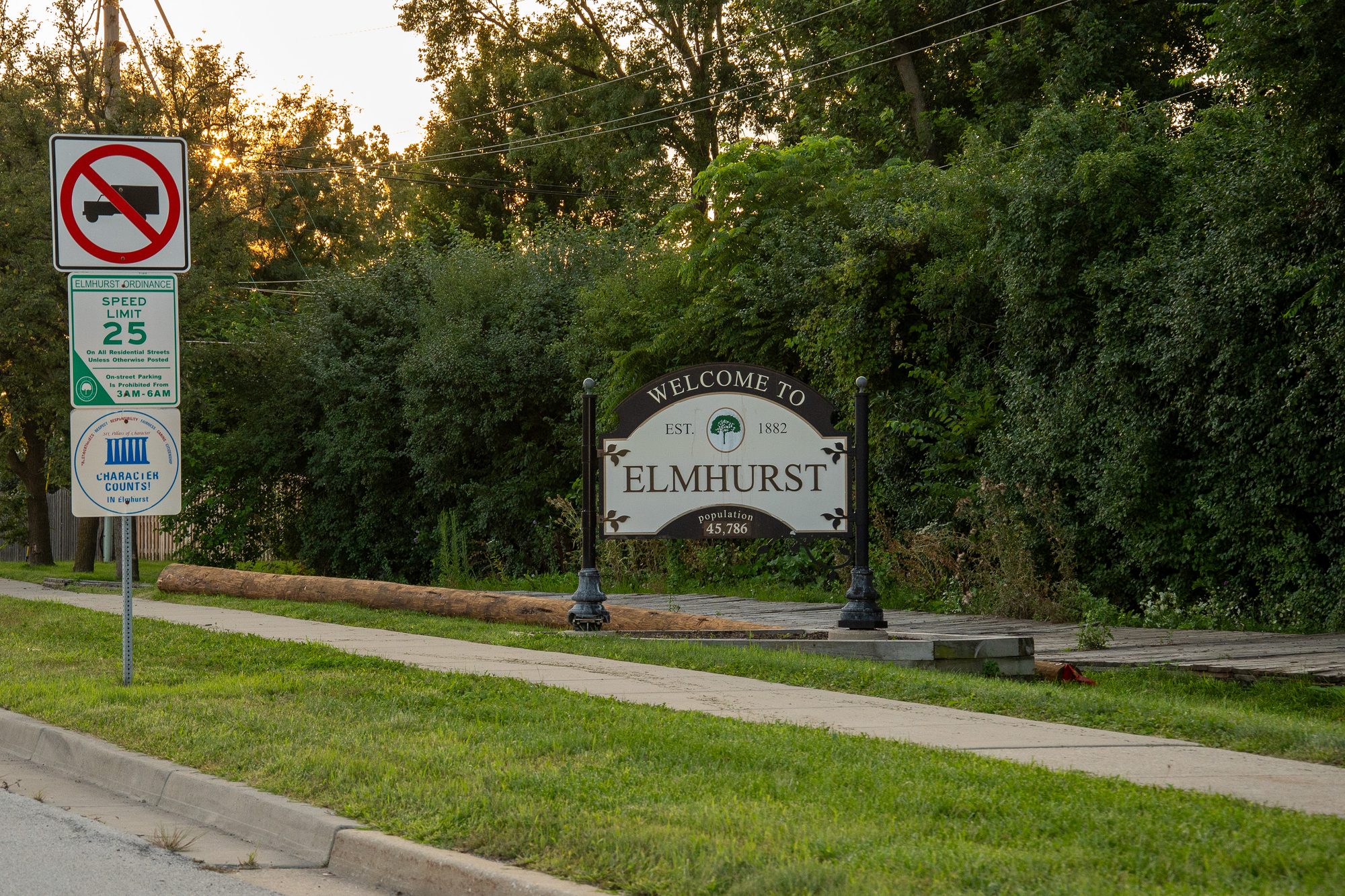 Decorative welcome sign for a city along a tree-lined road at dusk.