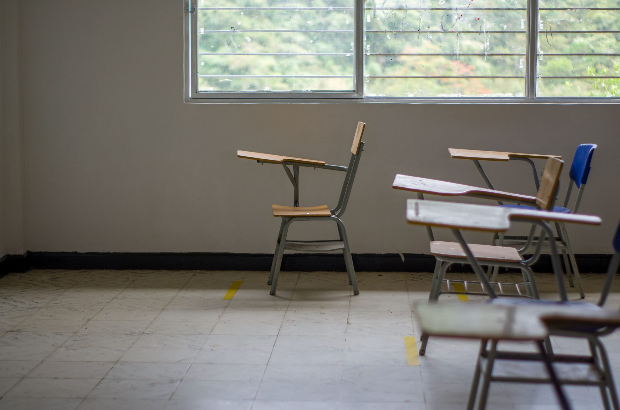 An empty classroom with rows of desks beside a large window.