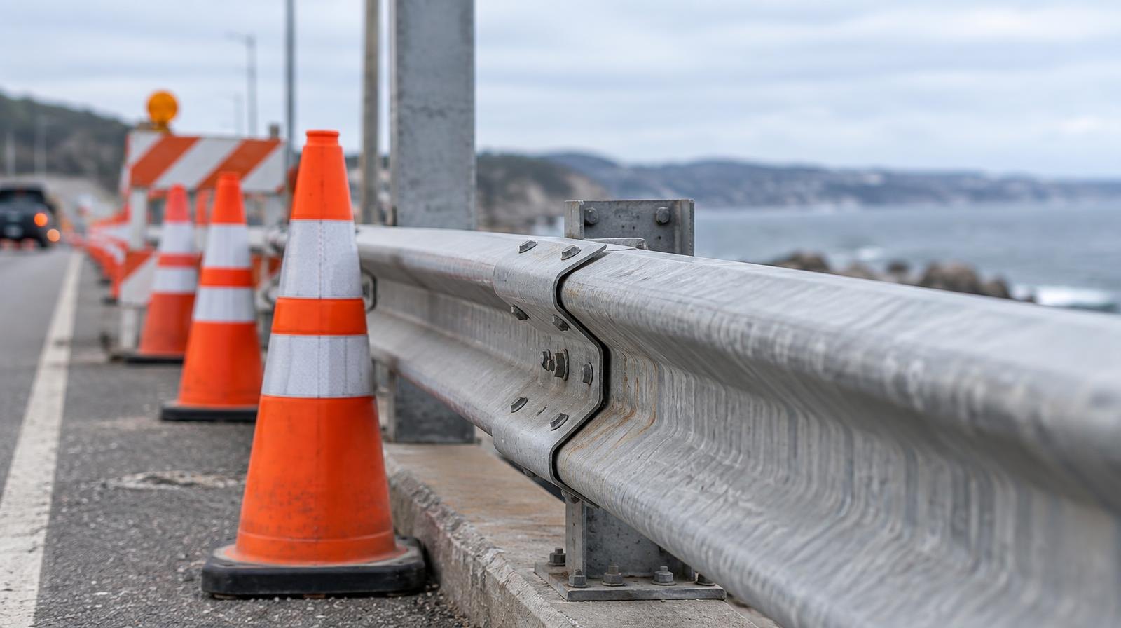 Metal bridge guardrail along a road with orange traffic cones and construction barriers.